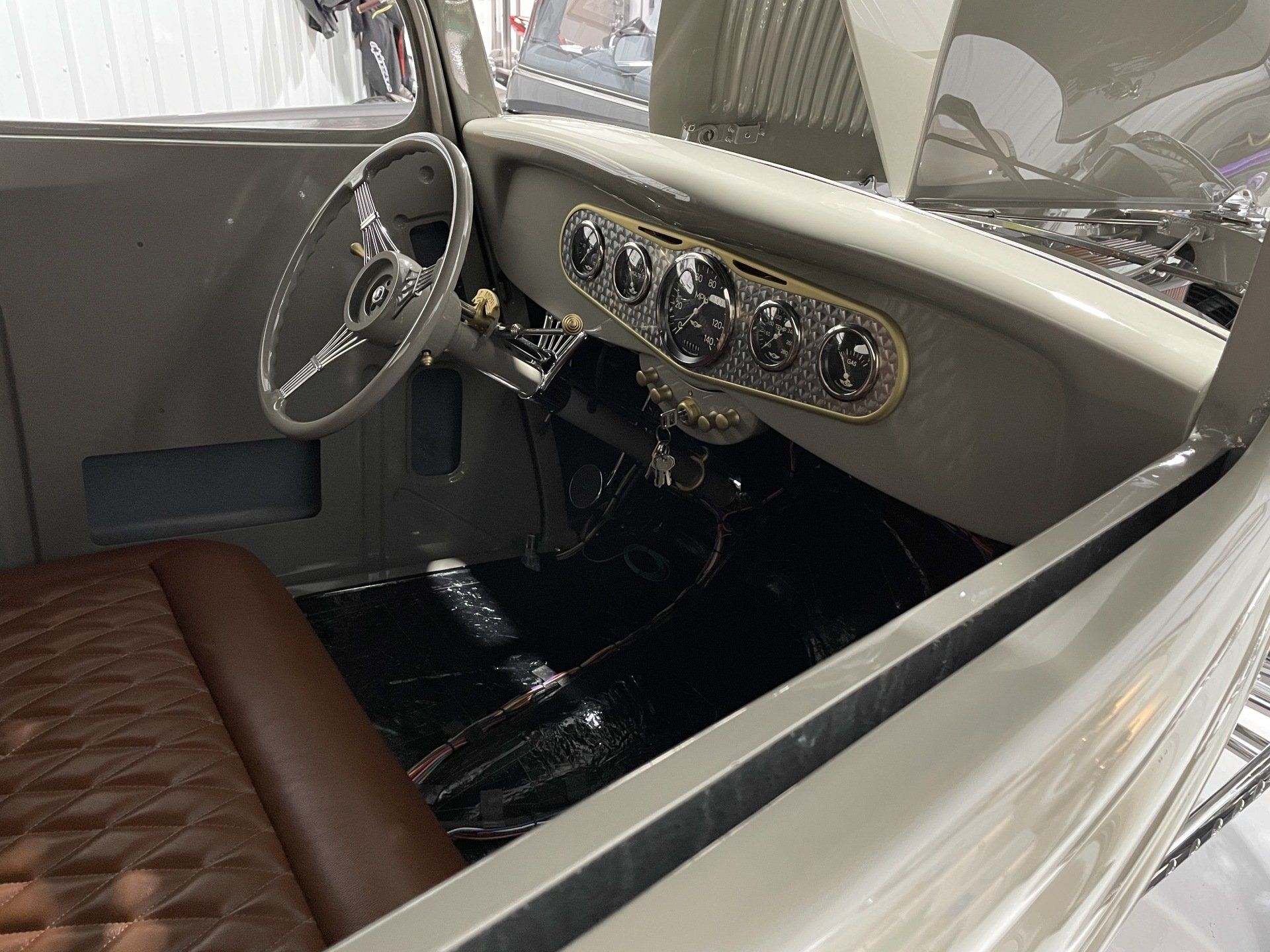 Vintage car interior with beige dashboard, chrome gauges, steering wheel, and brown quilted seat
