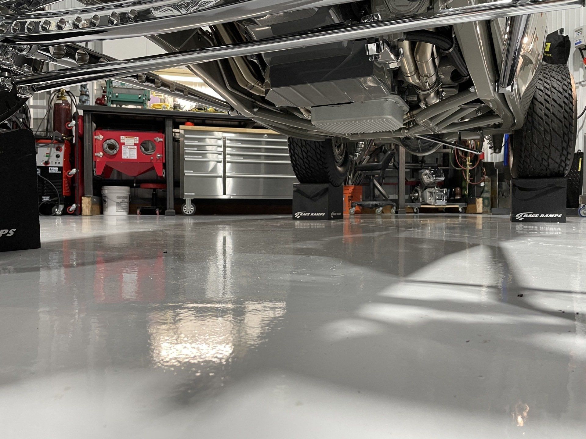Underbody view of a car in a garage, showing suspension, wheels, and a polished concrete floor.