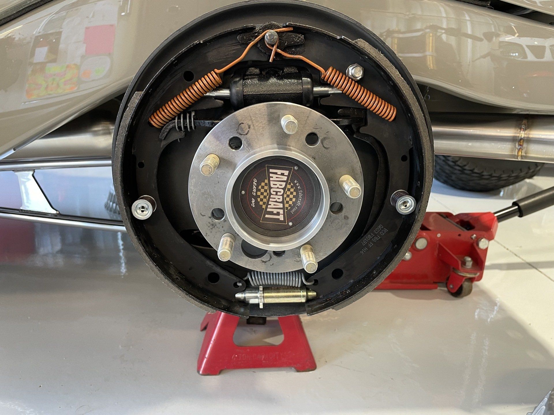 Close-up of a car’s exposed drum brake assembly with wheel removed, mounted on a red jack stand.