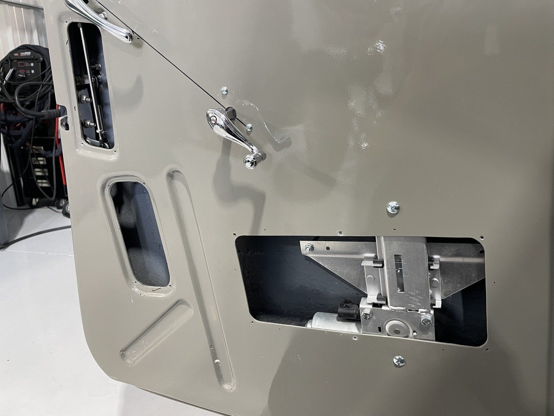 Close-up of a beige metal panel with cutouts, wiring, and a small latch mechanism mounted in a rectangular opening