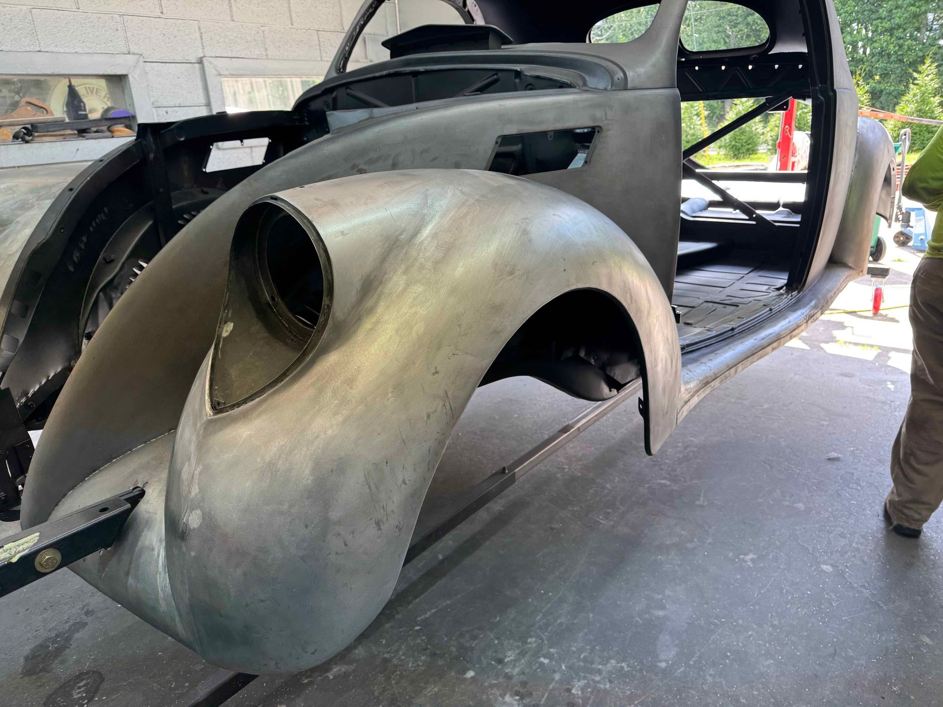Partially restored vintage car body in a garage, with bare metal fenders and open interior