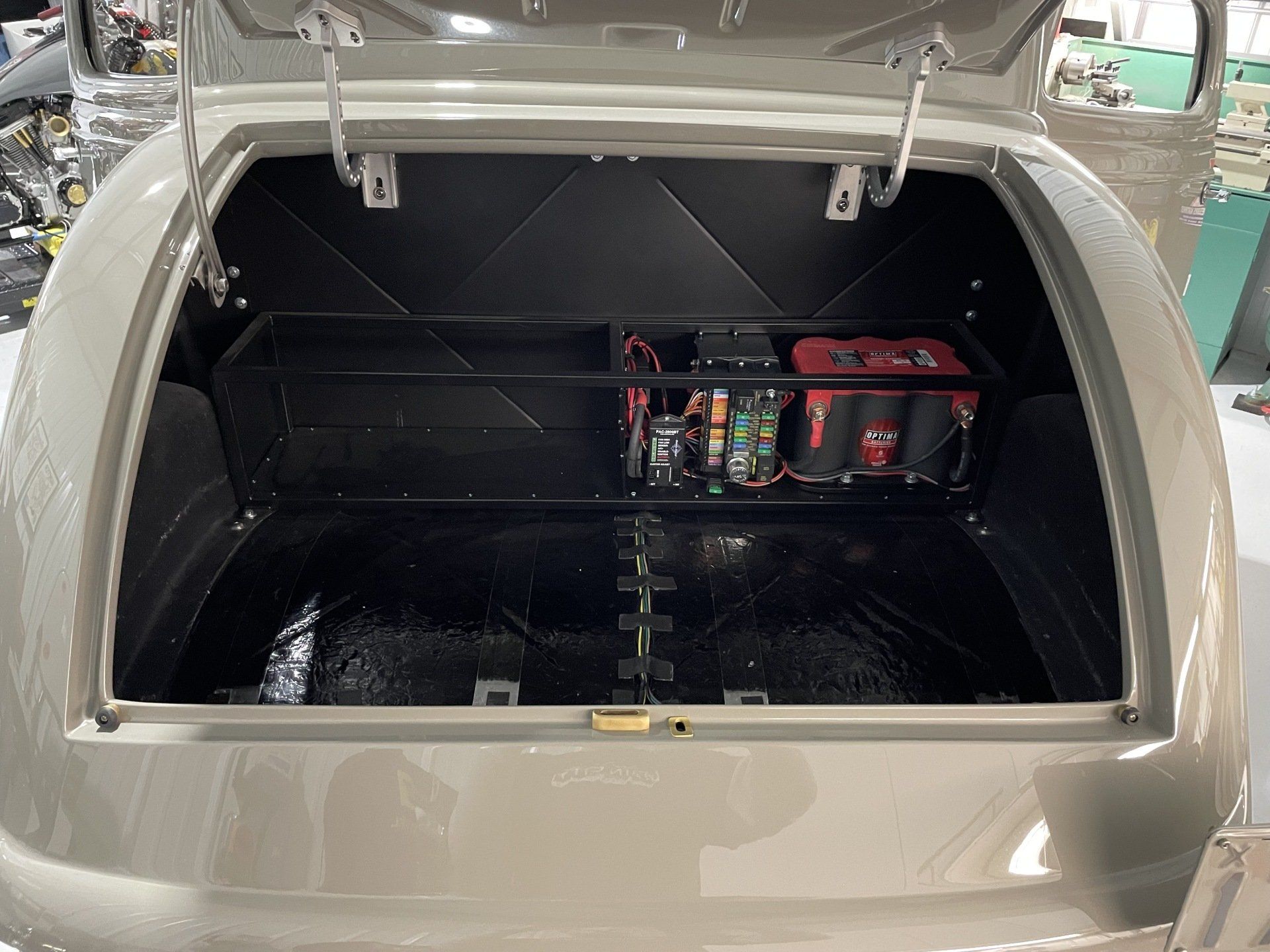 Open car trunk with custom black storage compartment and red electrical equipment inside