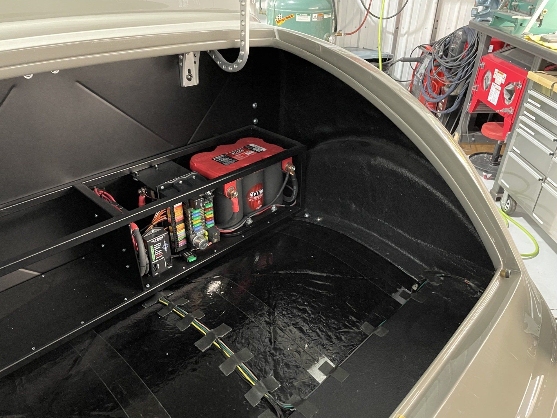 Open storage compartment with battery pack and wiring inside a black-and-tan vehicle body