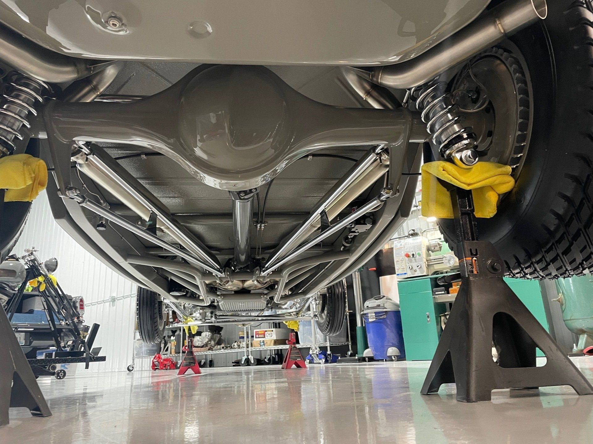 Undercarriage of a car lifted in a workshop, with tools and stands visible on the floor