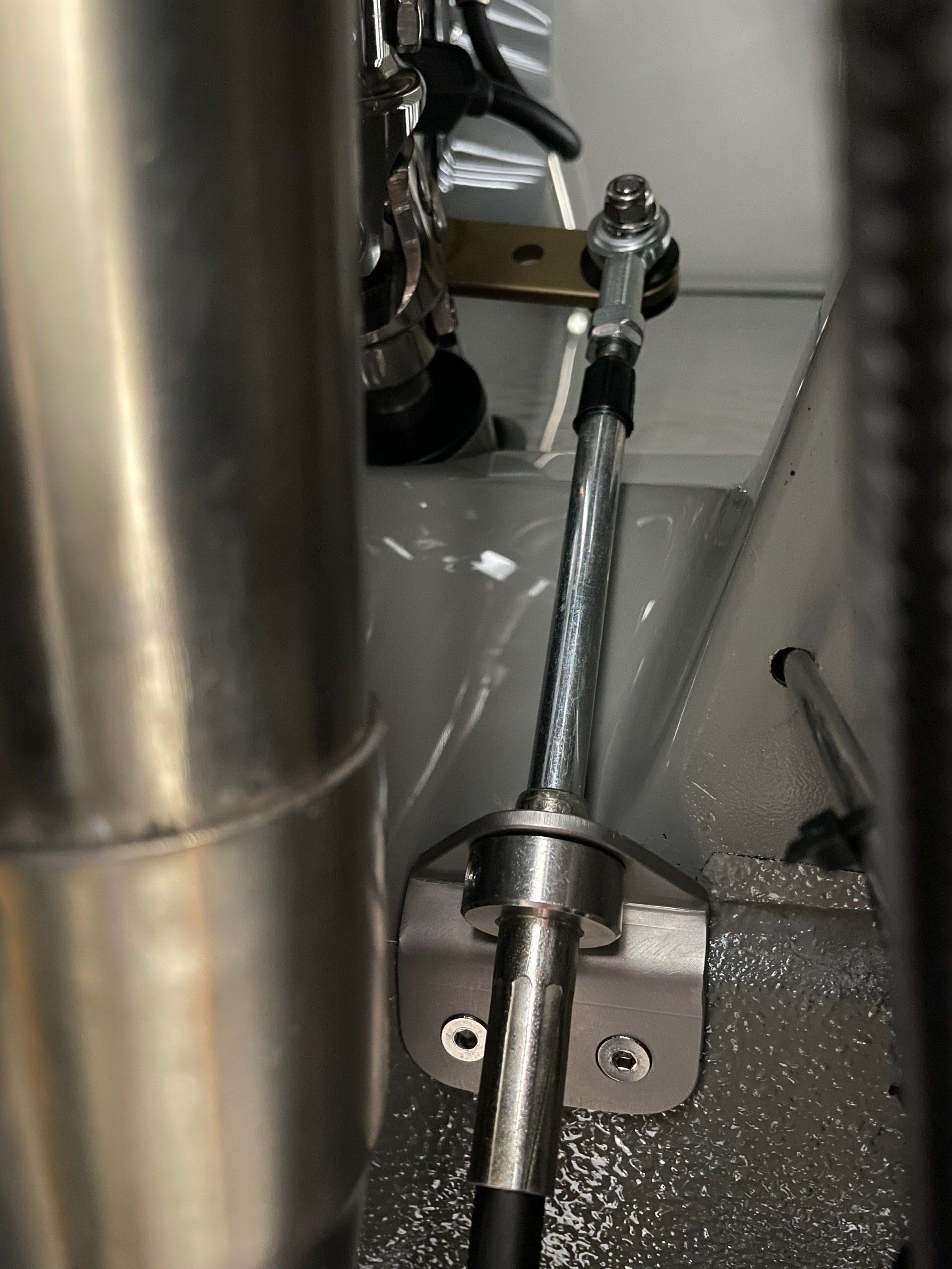 Close-up of a metal rod and hinge mechanism inside a gray industrial machine compartment