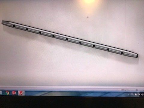 Metallic cylindrical bar with evenly spaced holes, lying diagonally on a light wall above a computer screen.