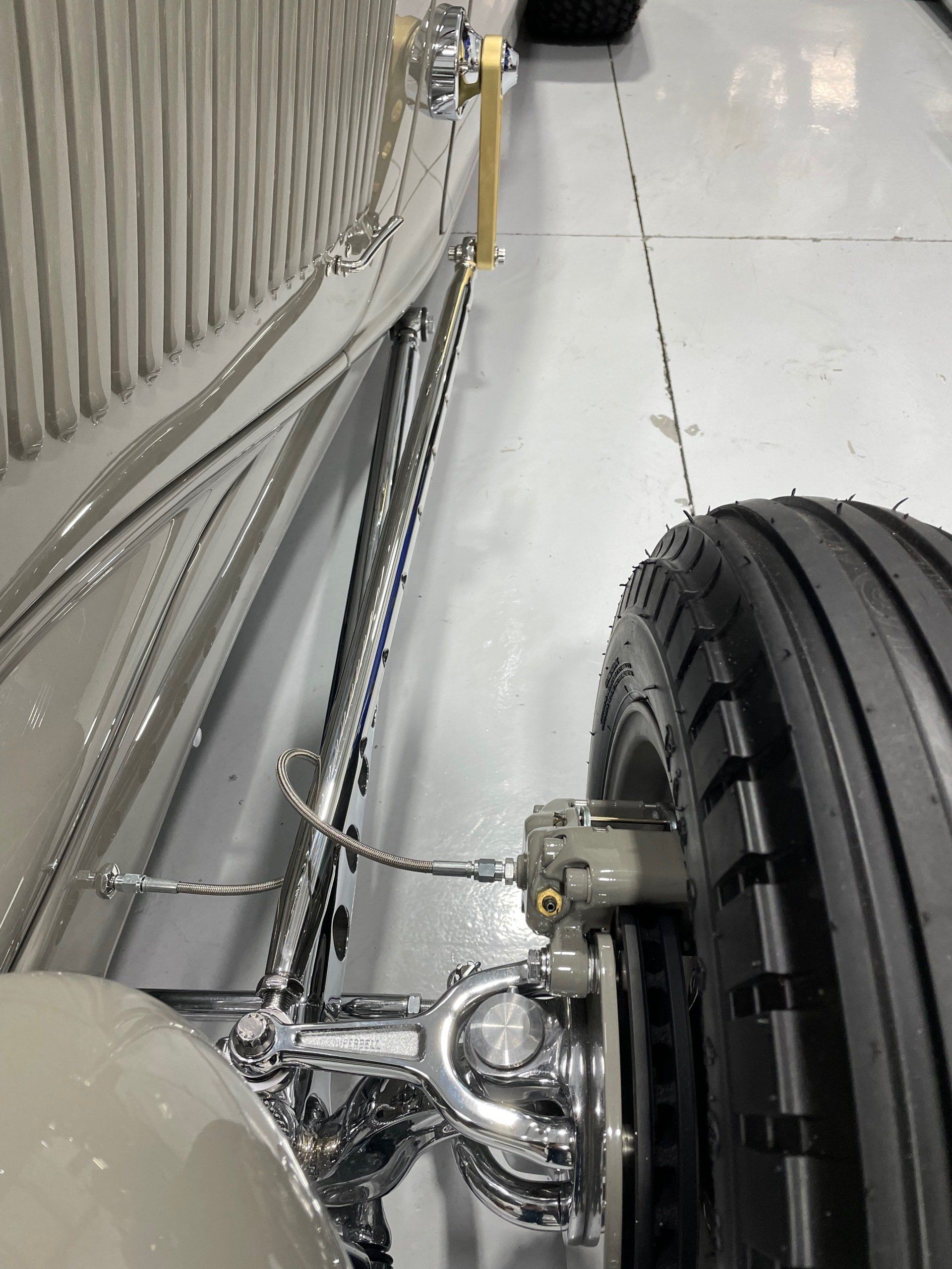 Close-up of a vehicle’s chrome suspension and front wheel on a glossy floor.