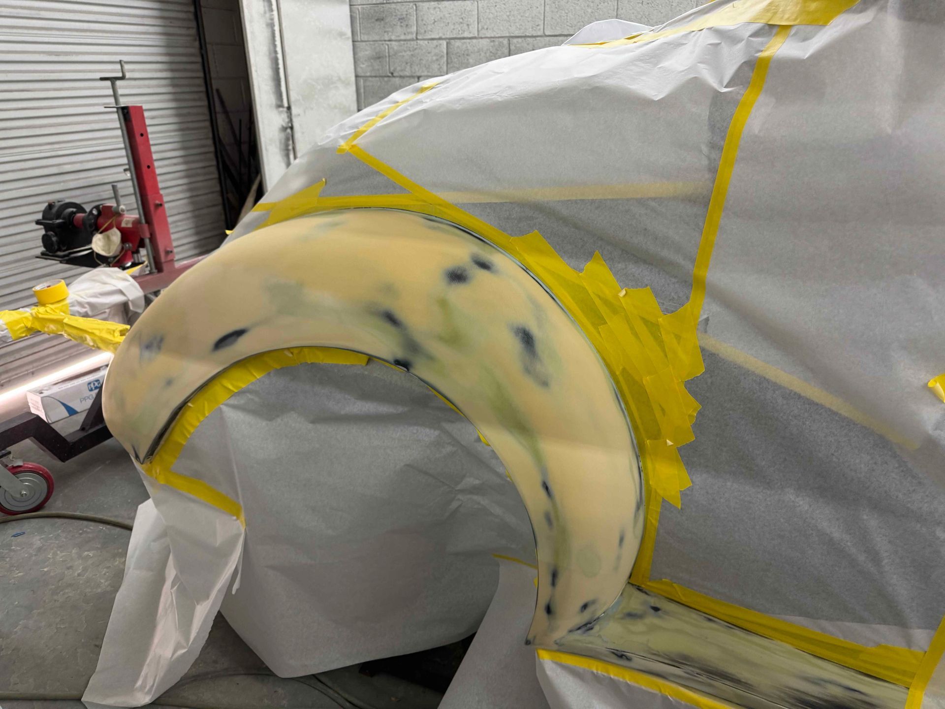 Masked car fender in auto body shop, covered in yellow tape and plastic sheeting