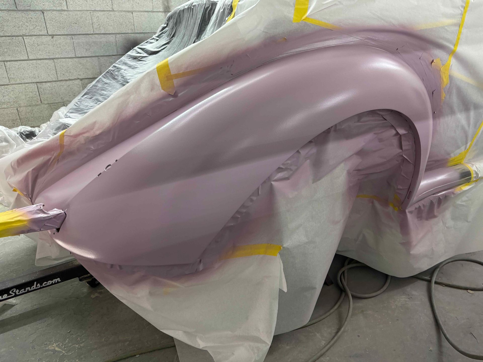 A mauve car body panel masked with plastic and tape in a workshop during paint prep