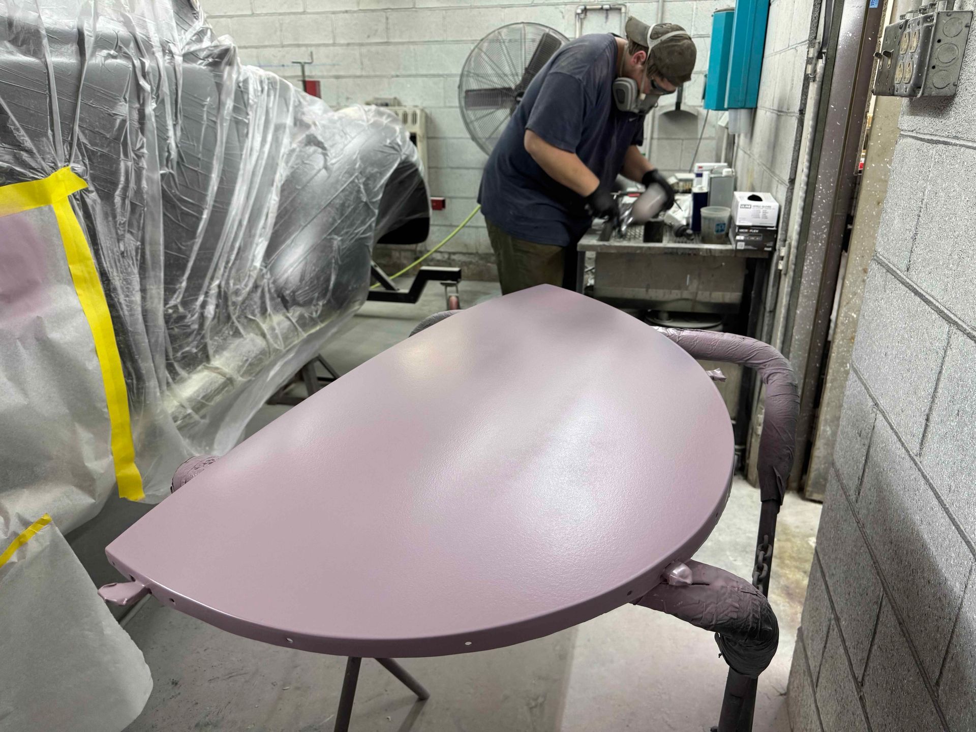 Technician working in a workshop beside a large purple curved plastic part on a stand