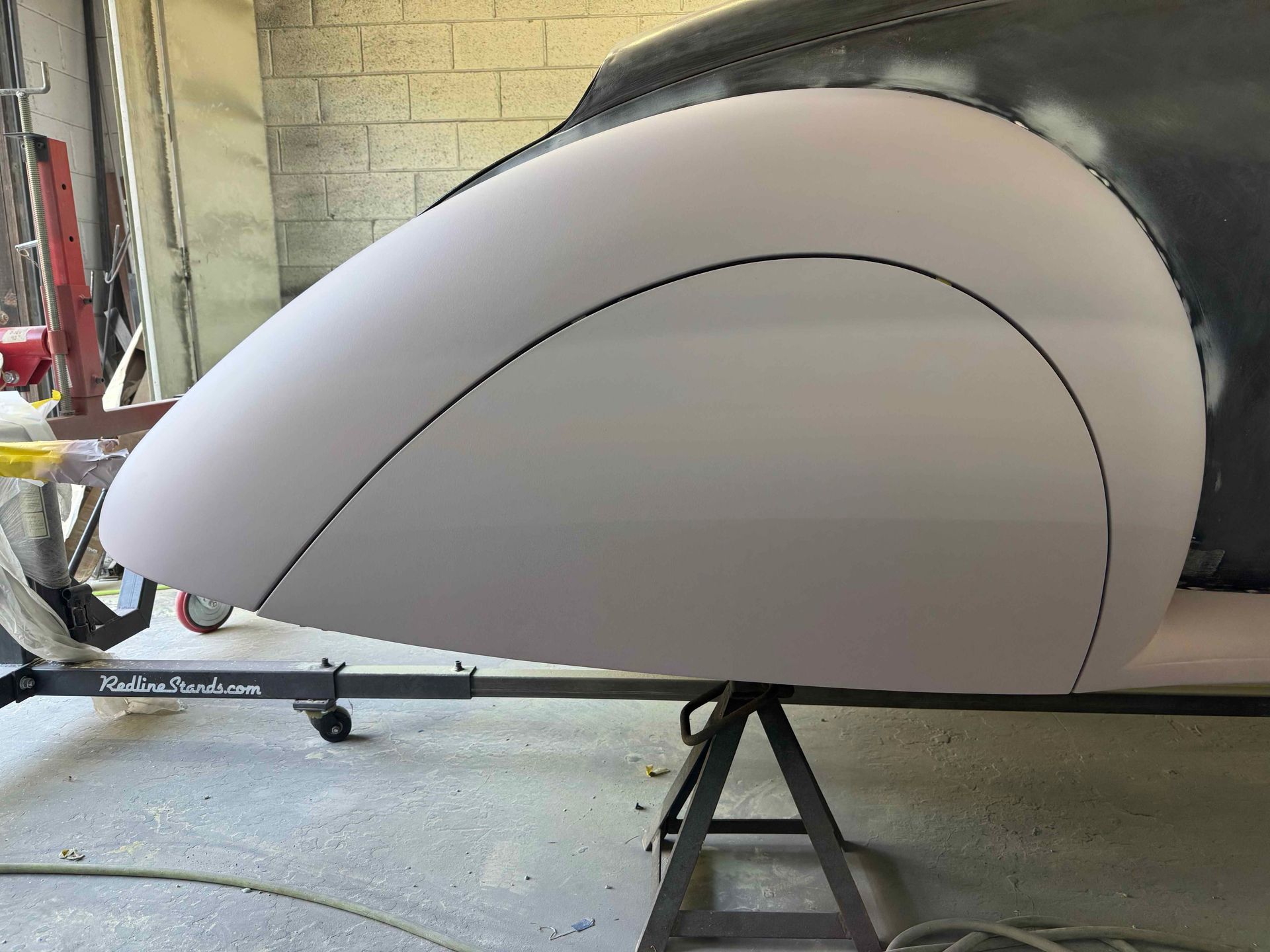 Gray aircraft nose cone in a workshop, supported on a stand with a curved black outline.