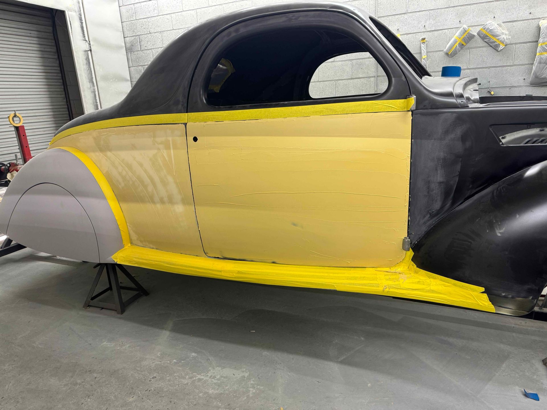 Partially restored vintage car body in a garage, with yellow primer and gray front and rear fenders
