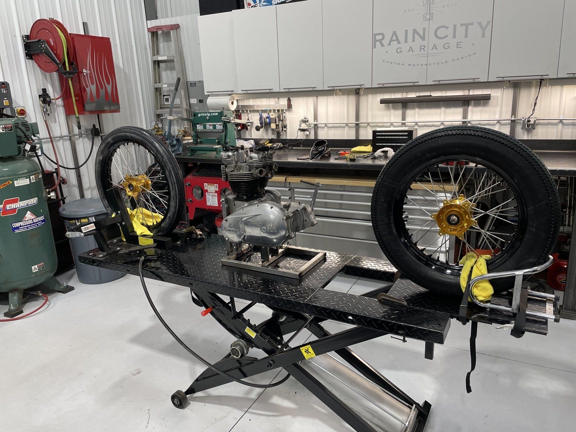 Motorcycle frame on a lift in a workshop, with wheels and tools around it