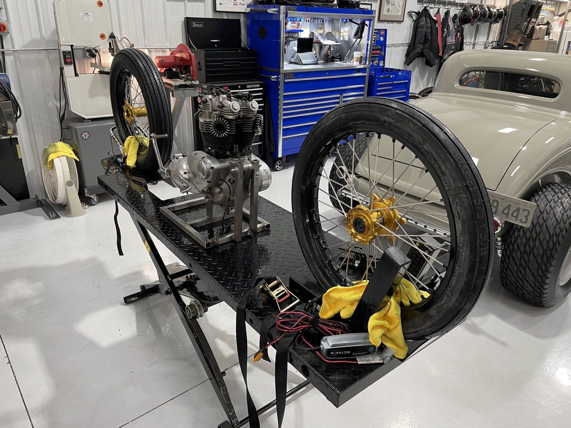 Custom-built motorcycle frame with two large wheels in a workshop, near tools and a blue tool chest