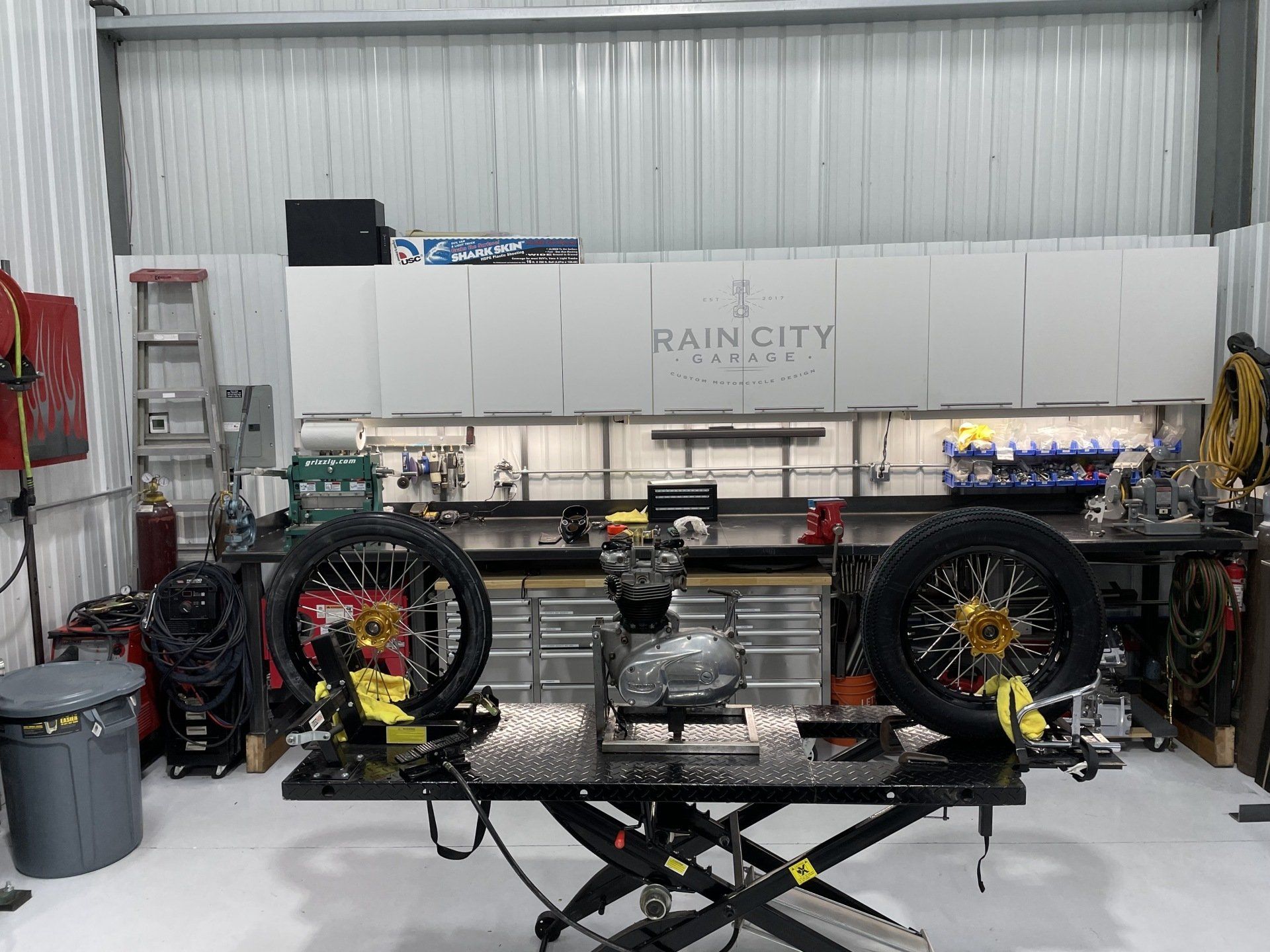 Workshop garage with a custom off-road vehicle frame, large tires, and tools in the background
