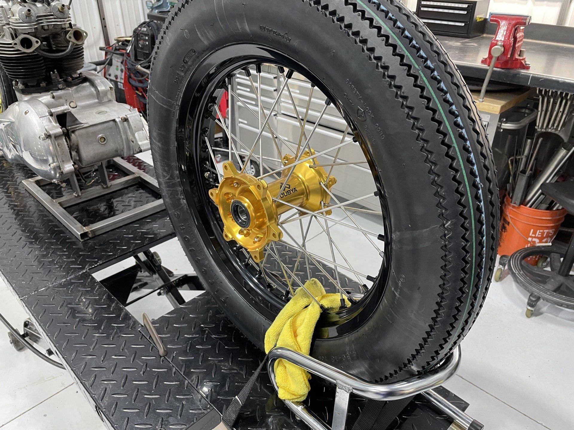 Large black motorcycle wheel with gold hub mounted on a workbench in a workshop
