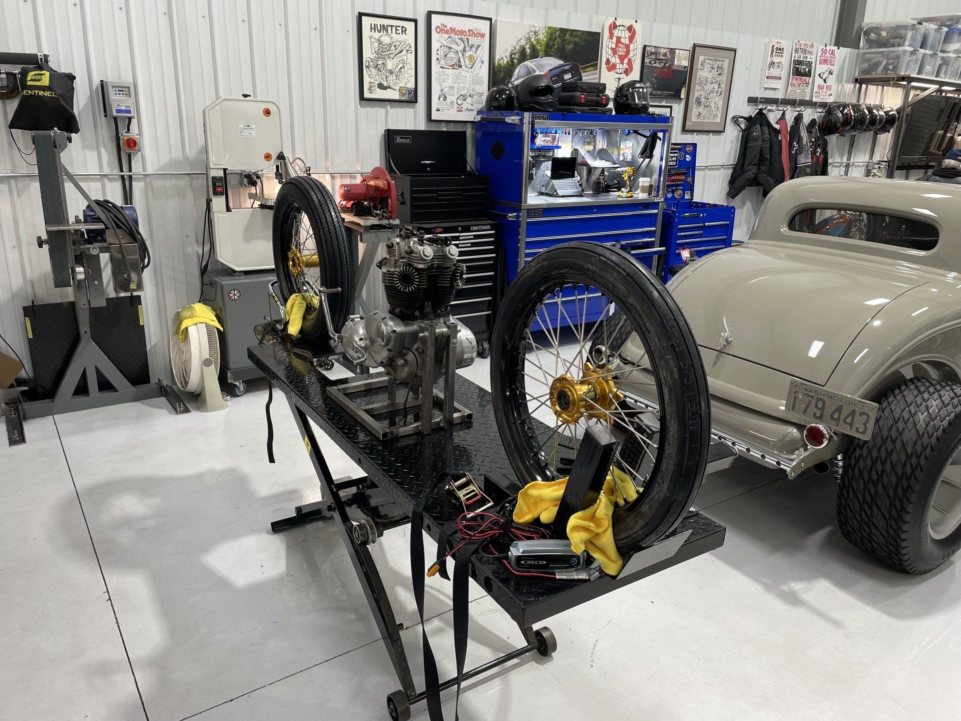 Custom car chassis in a garage with a beige hot rod body, exposed wheels, and tools in the background