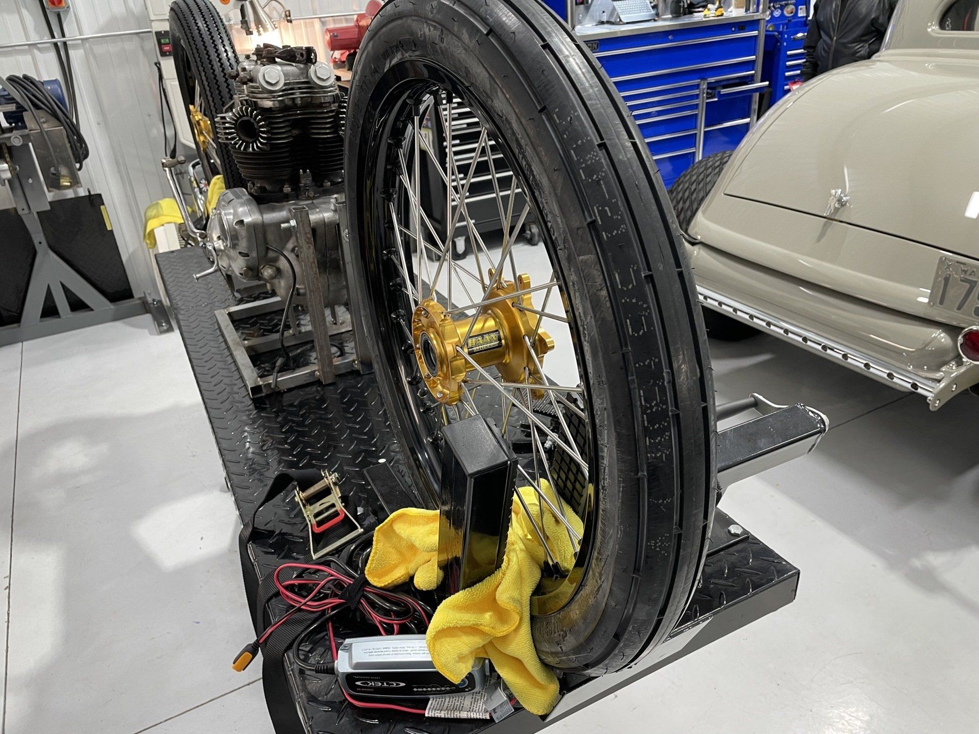 Close-up of a motorcycle wheel on a repair stand in a workshop, with tools and yellow gloves nearby.