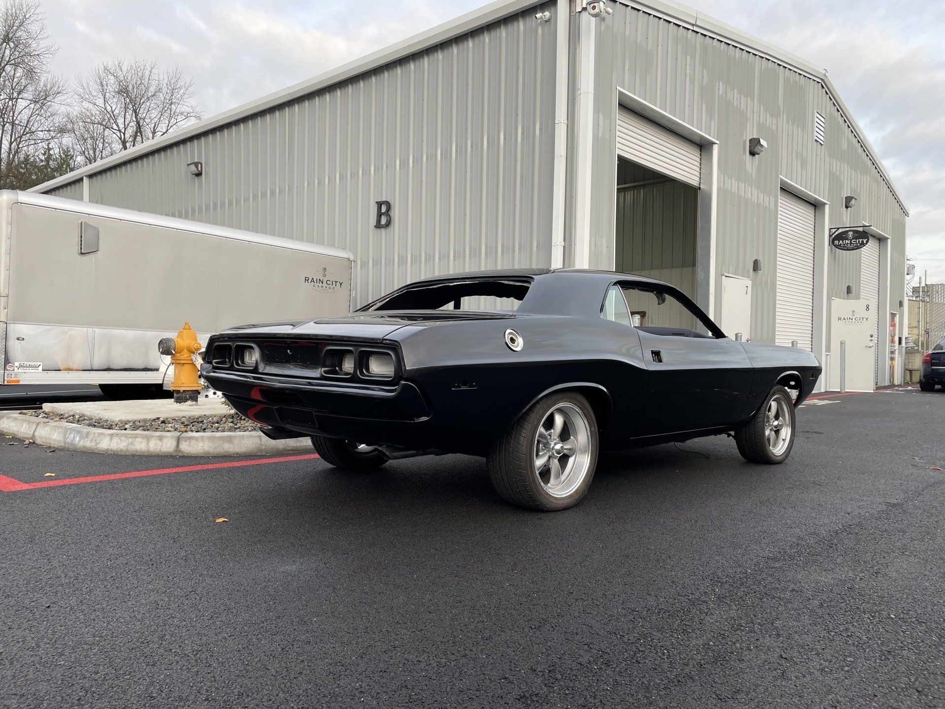 Black classic car parked outside a gray industrial warehouse