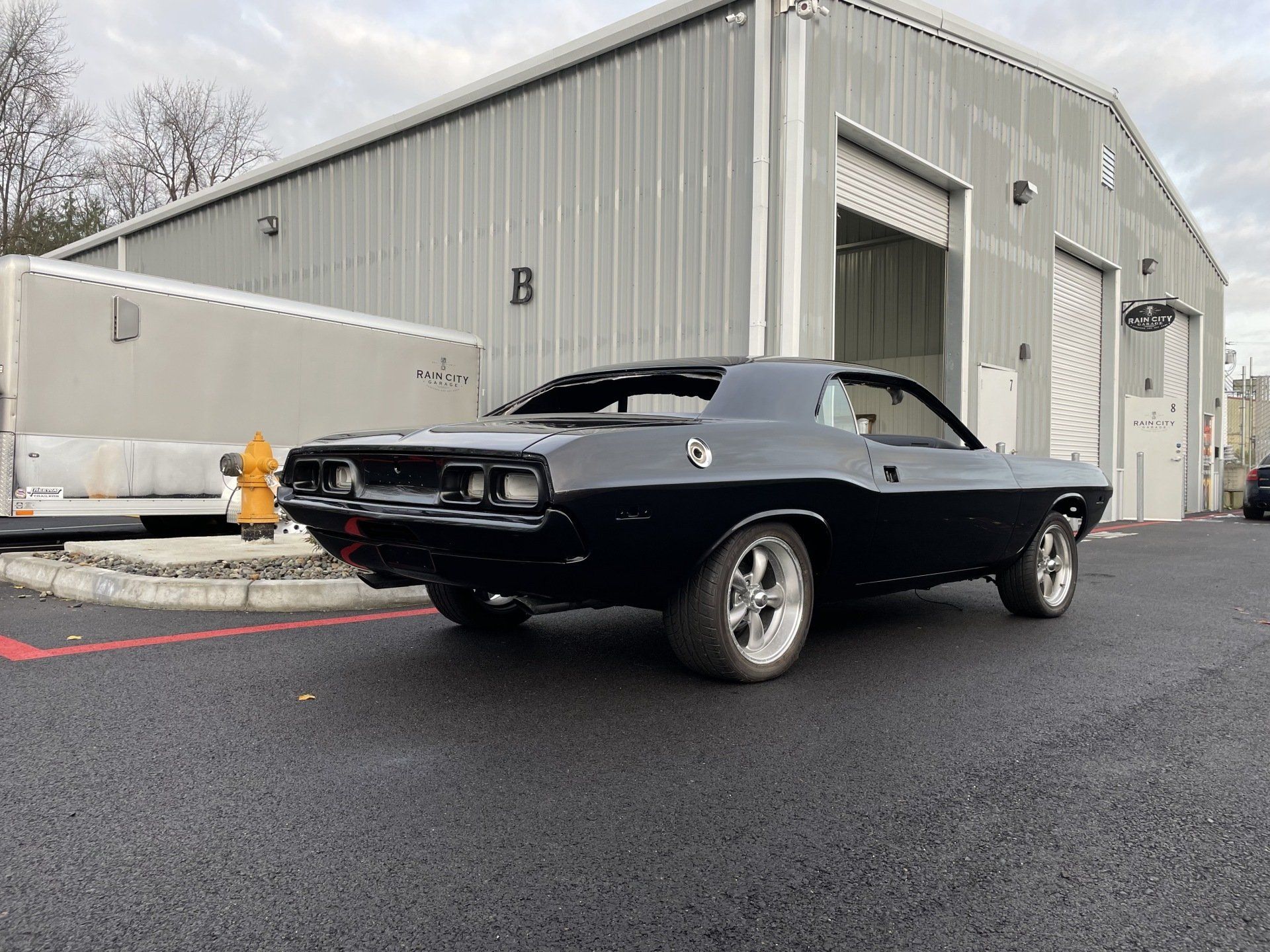 Classic black muscle car parked outside a gray industrial building.