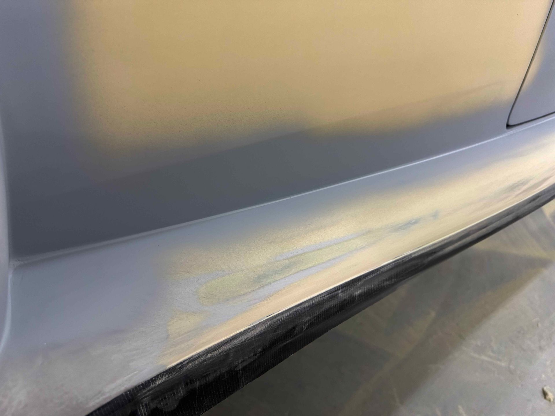 Close-up of a scratched silver car bumper with yellow scuff marks and a black trim edge