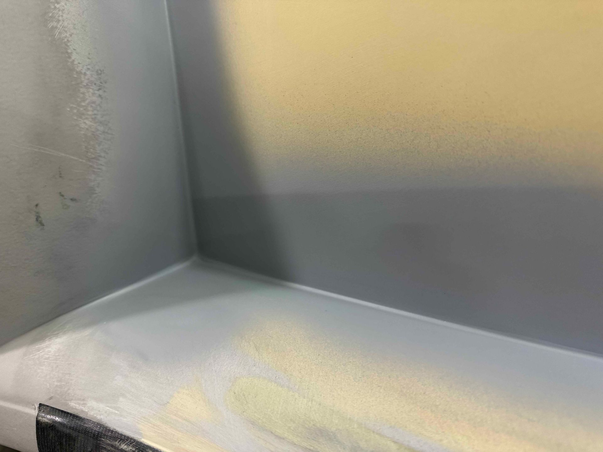 Close-up of a gray and yellow painted corner with a white ledge and a small black taped section.