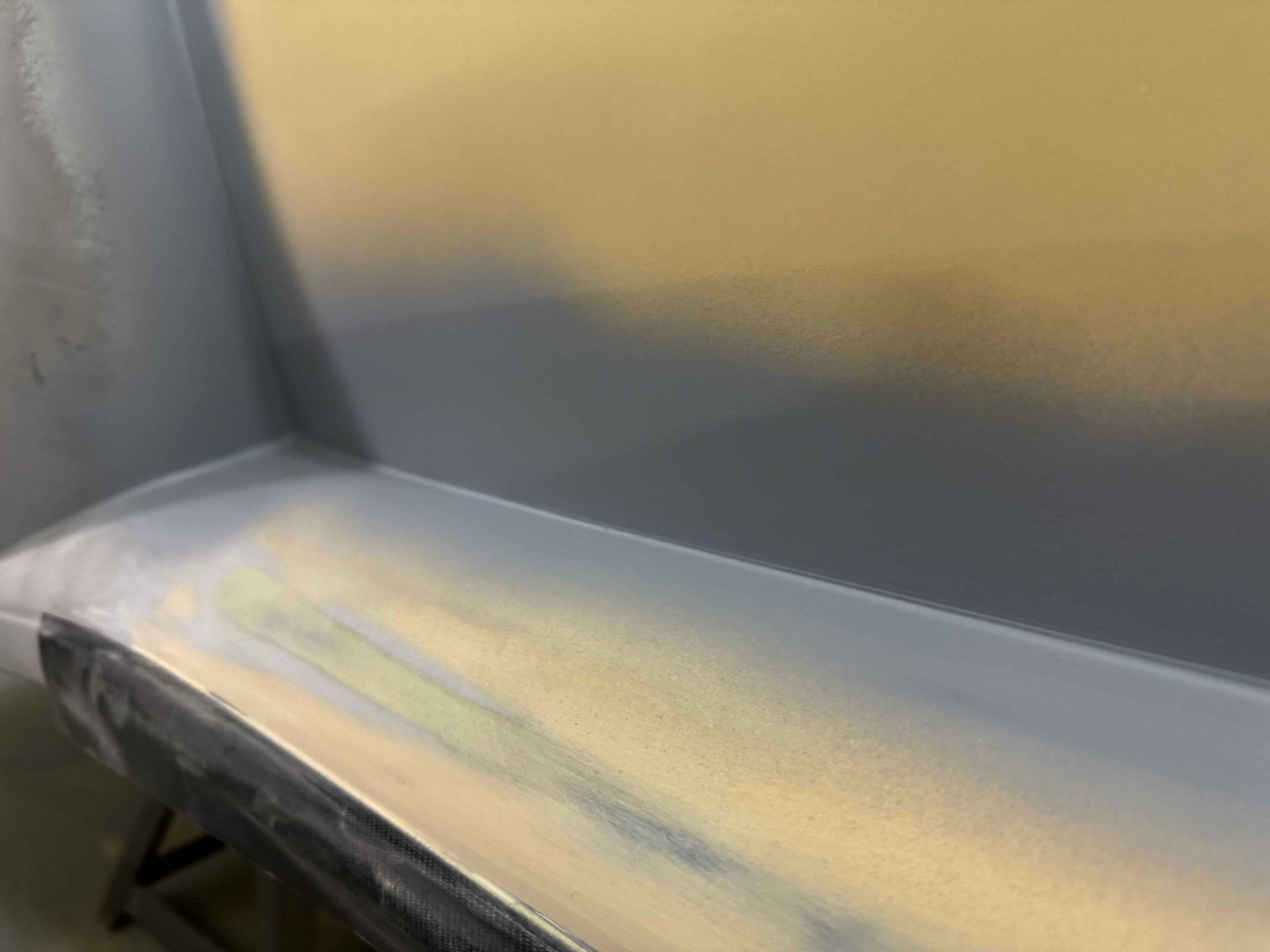 Close-up of a gray and beige upholstered seat with a worn edge and metal frame