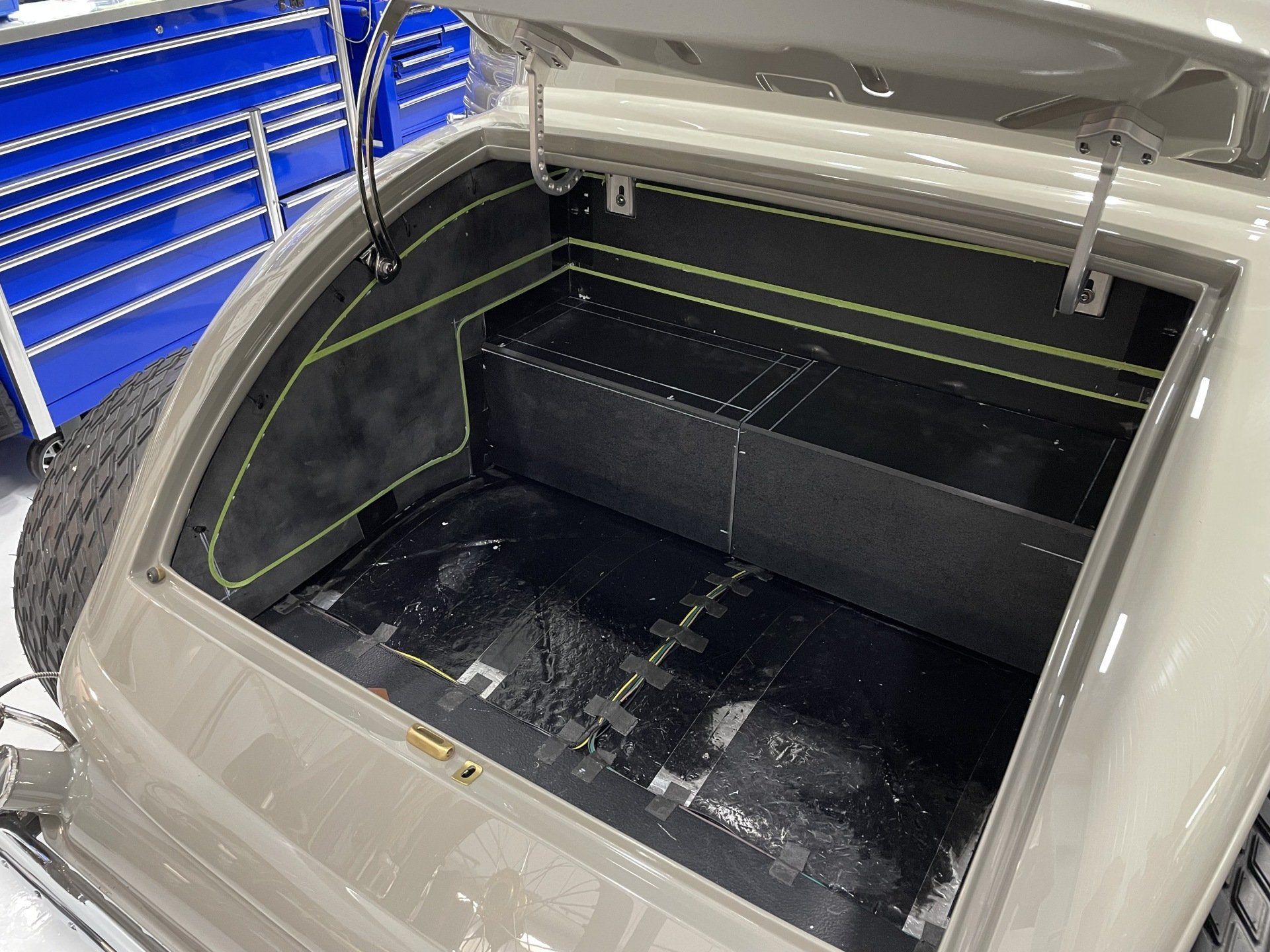 Open car trunk with black interior and beige exterior in a garage
