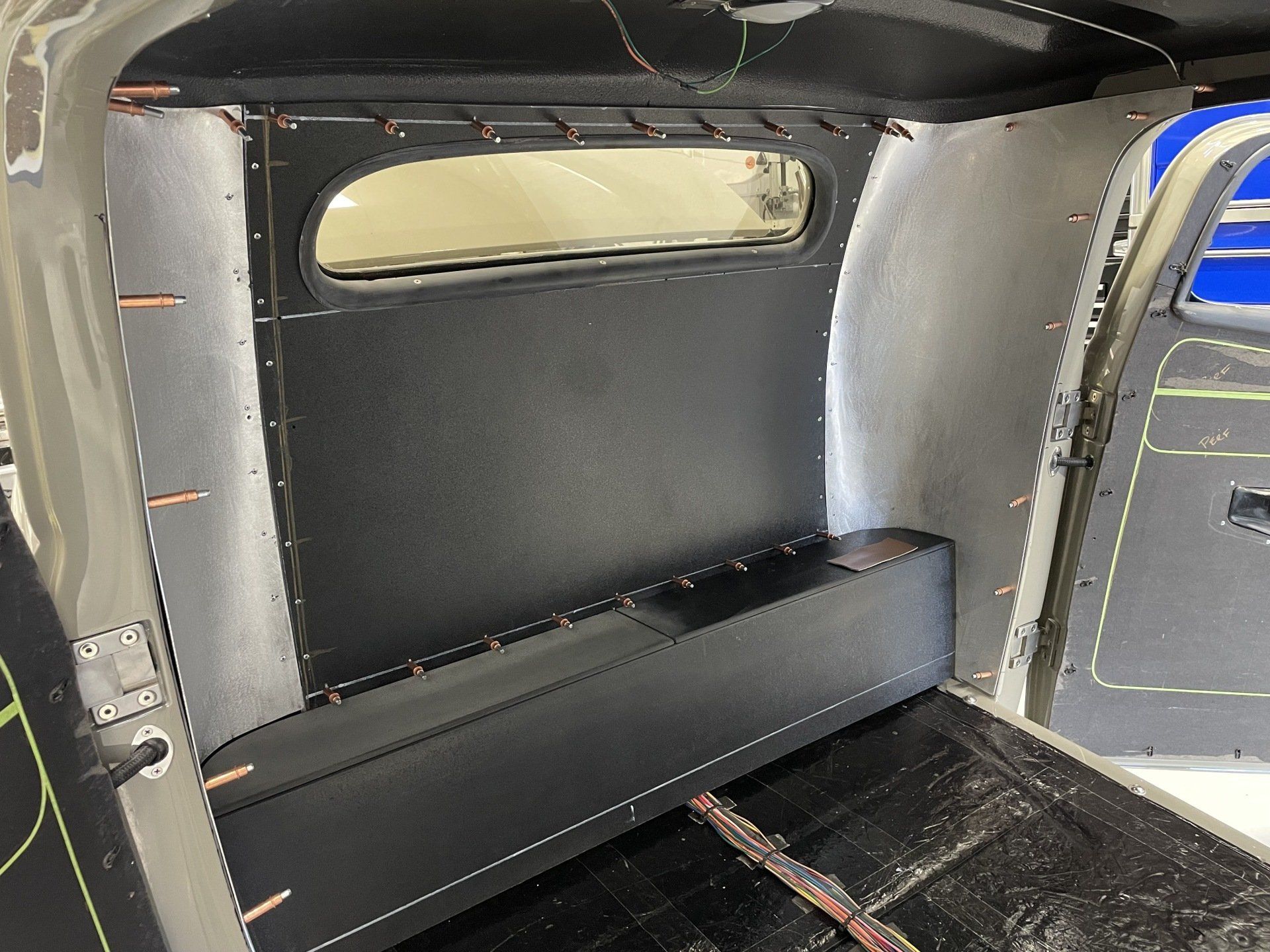 Interior of a van with a black bench seat and a small rear window, showing a compact custom setup.