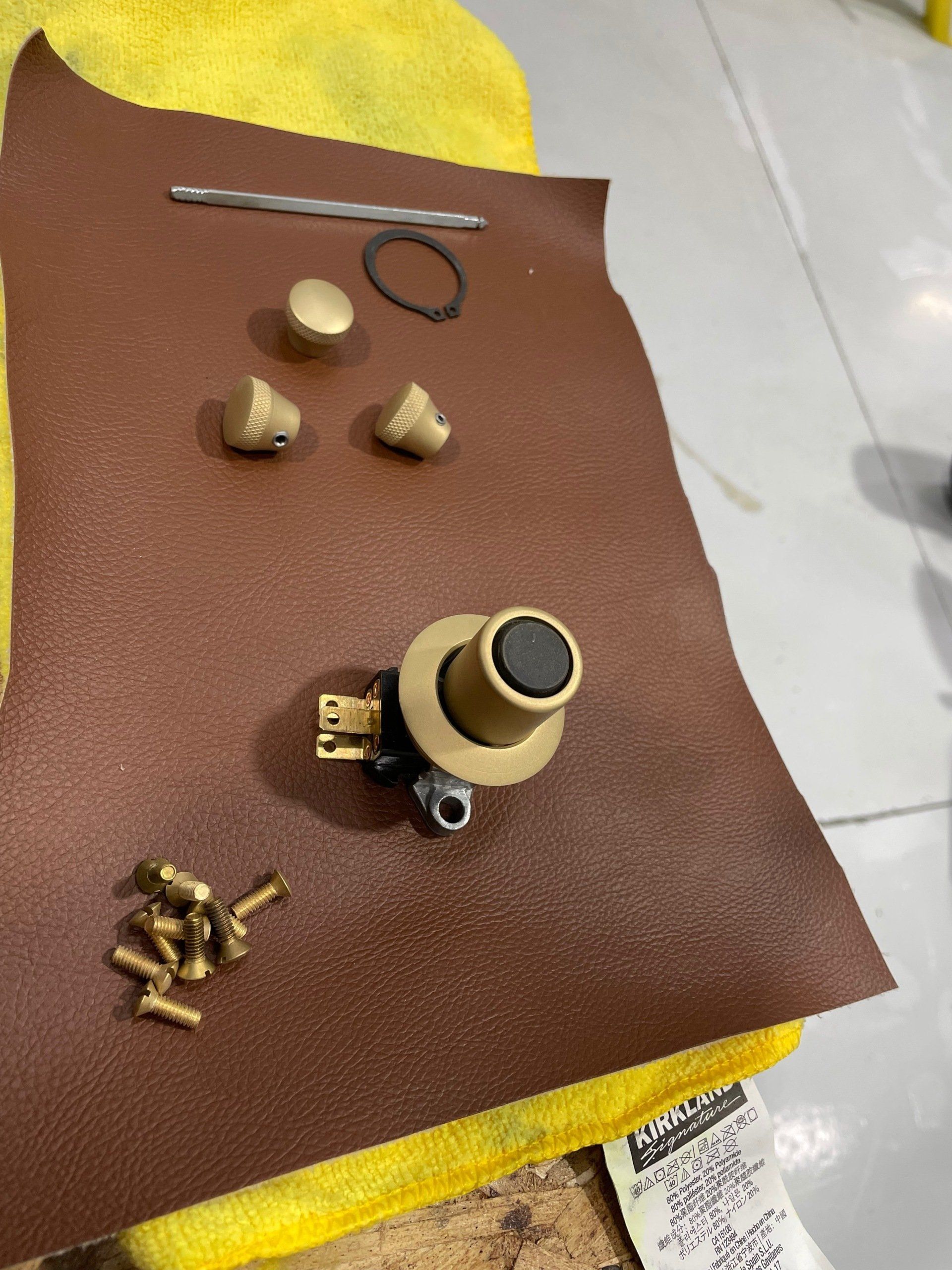 Assorted small brass-colored parts and a knob on brown sanding paper with yellow cloth edges