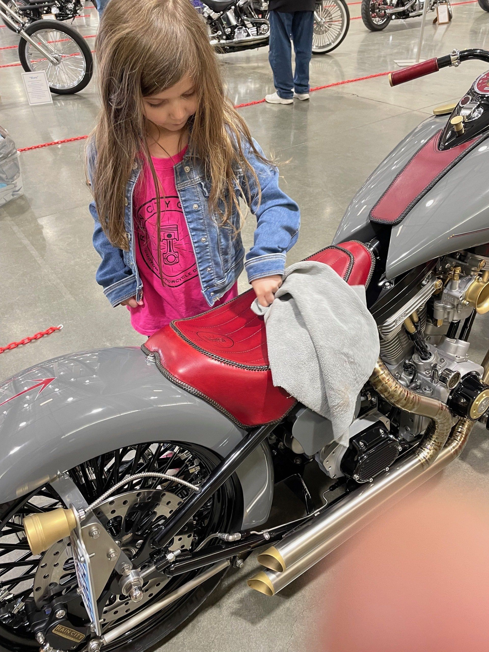 Girl standing beside a gray and red motorcycle, wiping it with a cloth in a wet outdoor setting