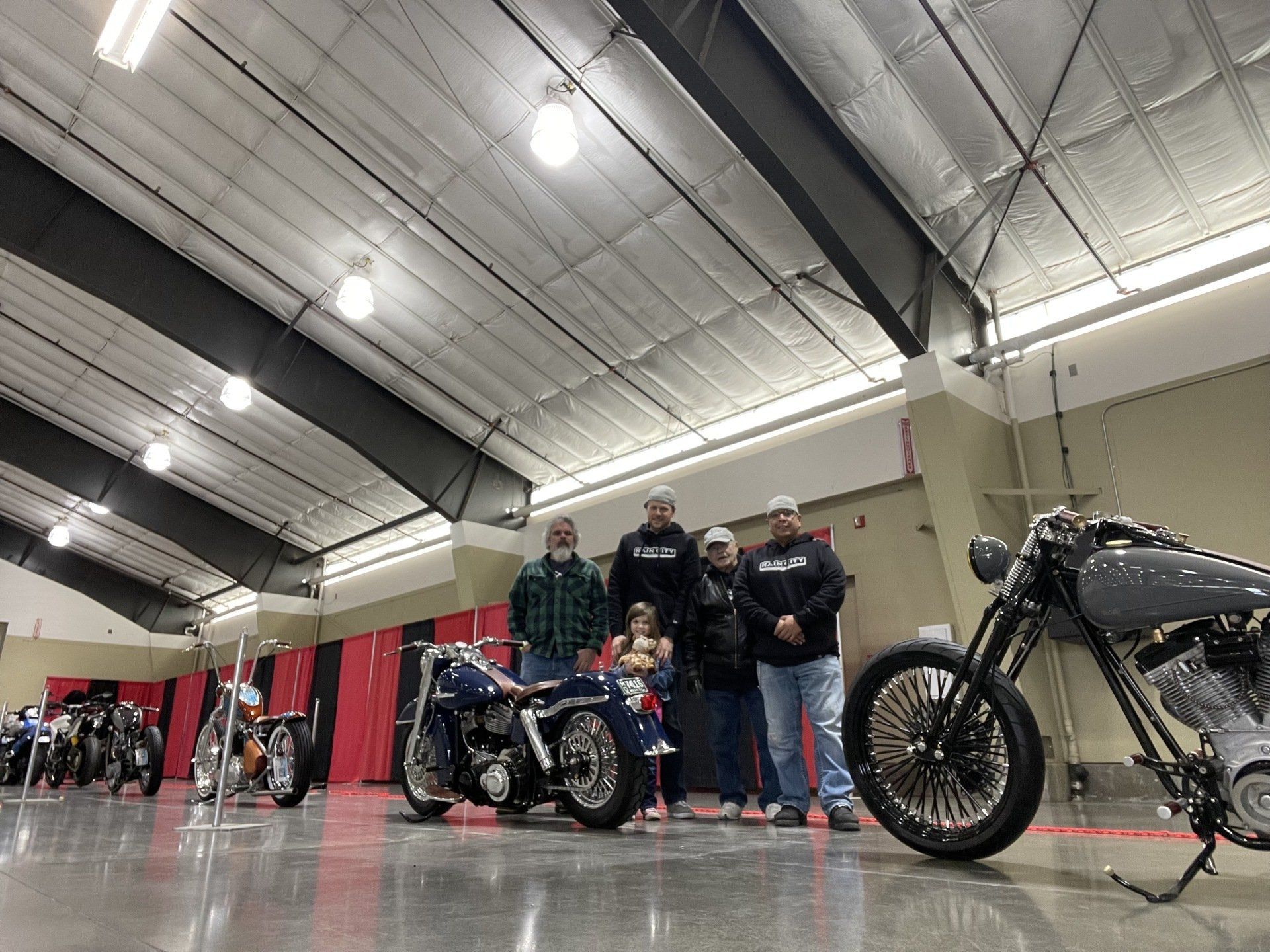 Motorcycles and people at an indoor bike show, with a black motorcycle in the foreground.