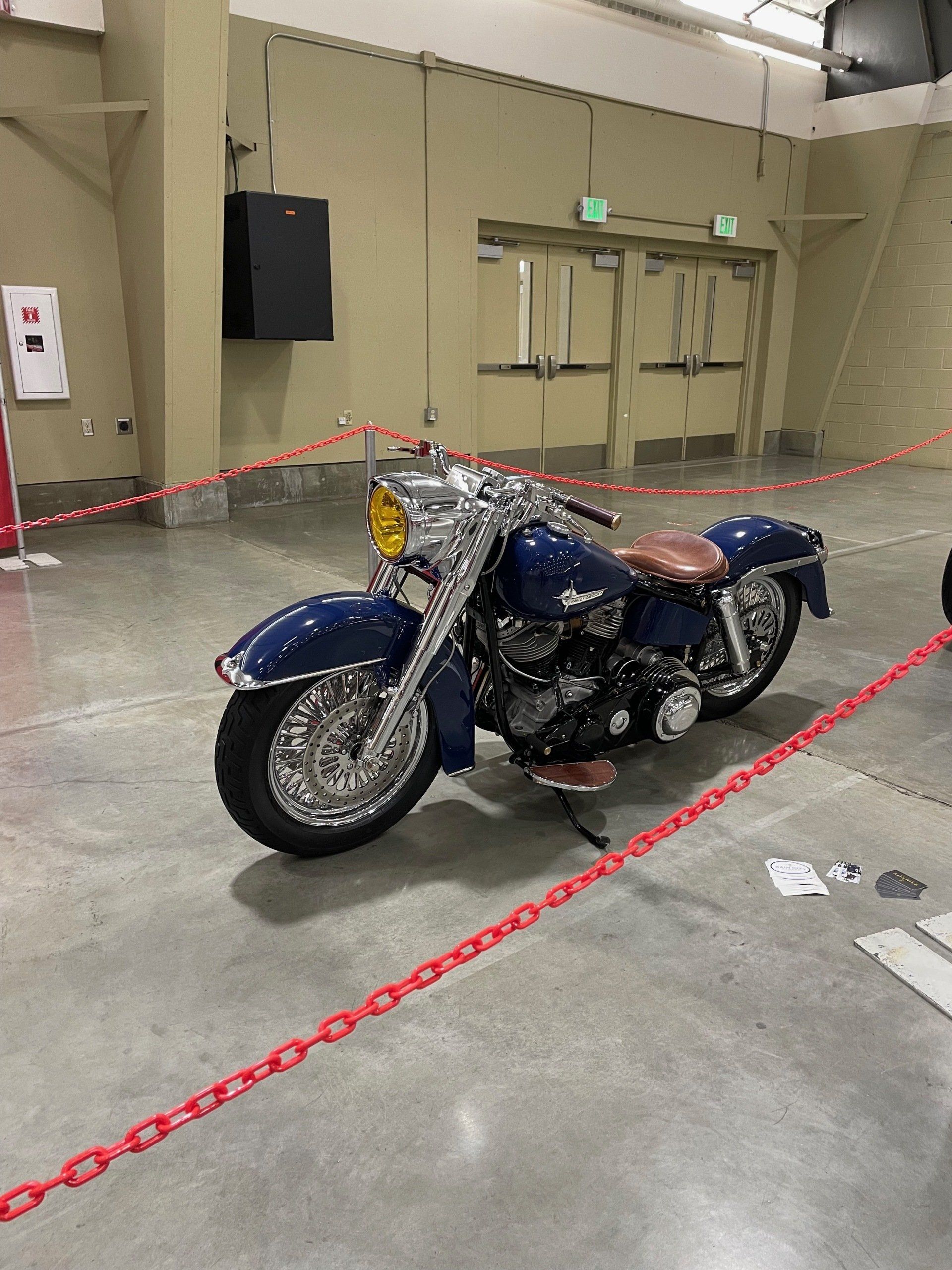 Blue motorcycle displayed inside a roped-off exhibition area in a large indoor hall