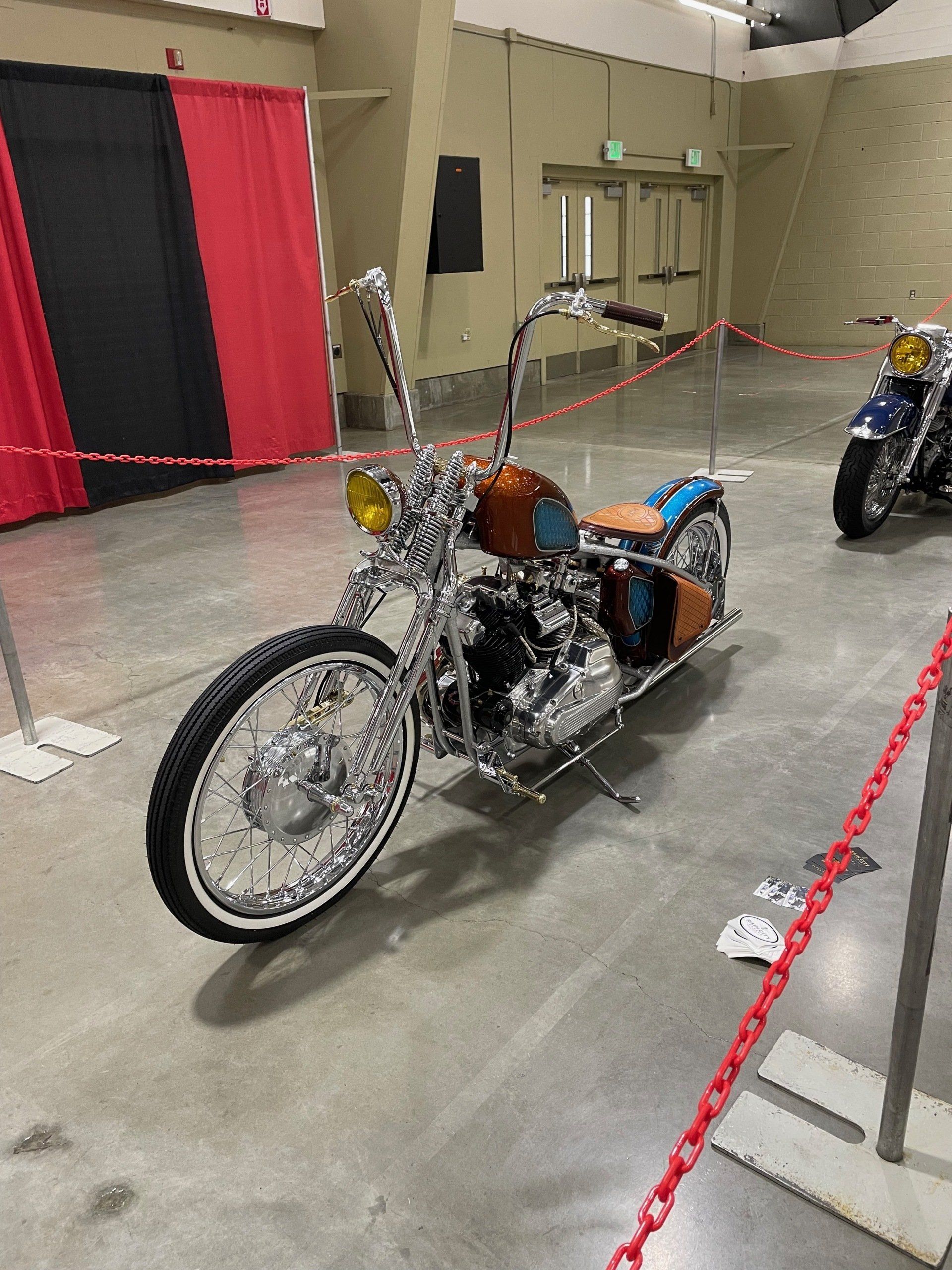 Custom chopper motorcycle on display behind red rope in an indoor exhibition hall