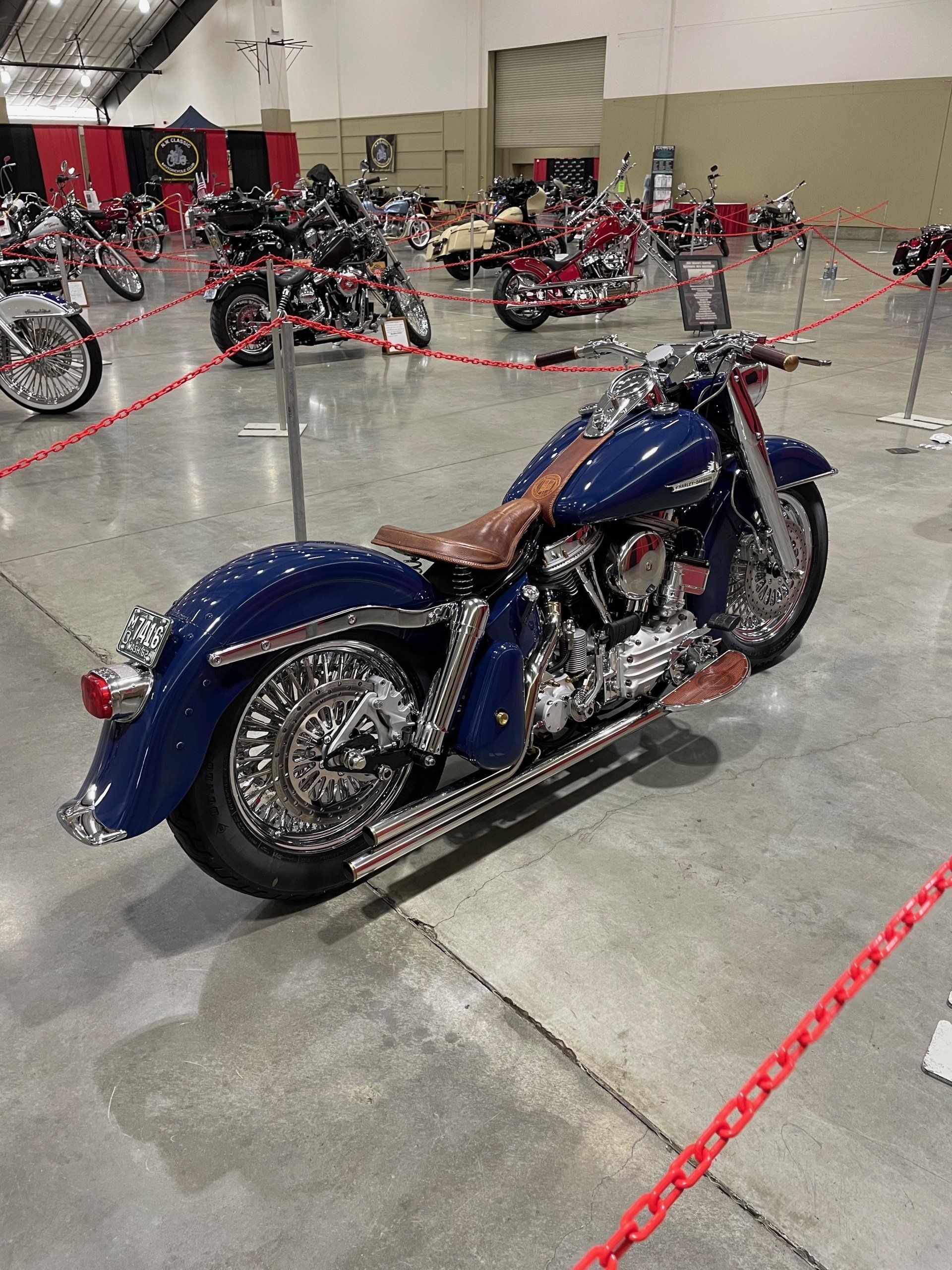 Blue cruiser motorcycle on display in an indoor showroom, with other bikes in the background.