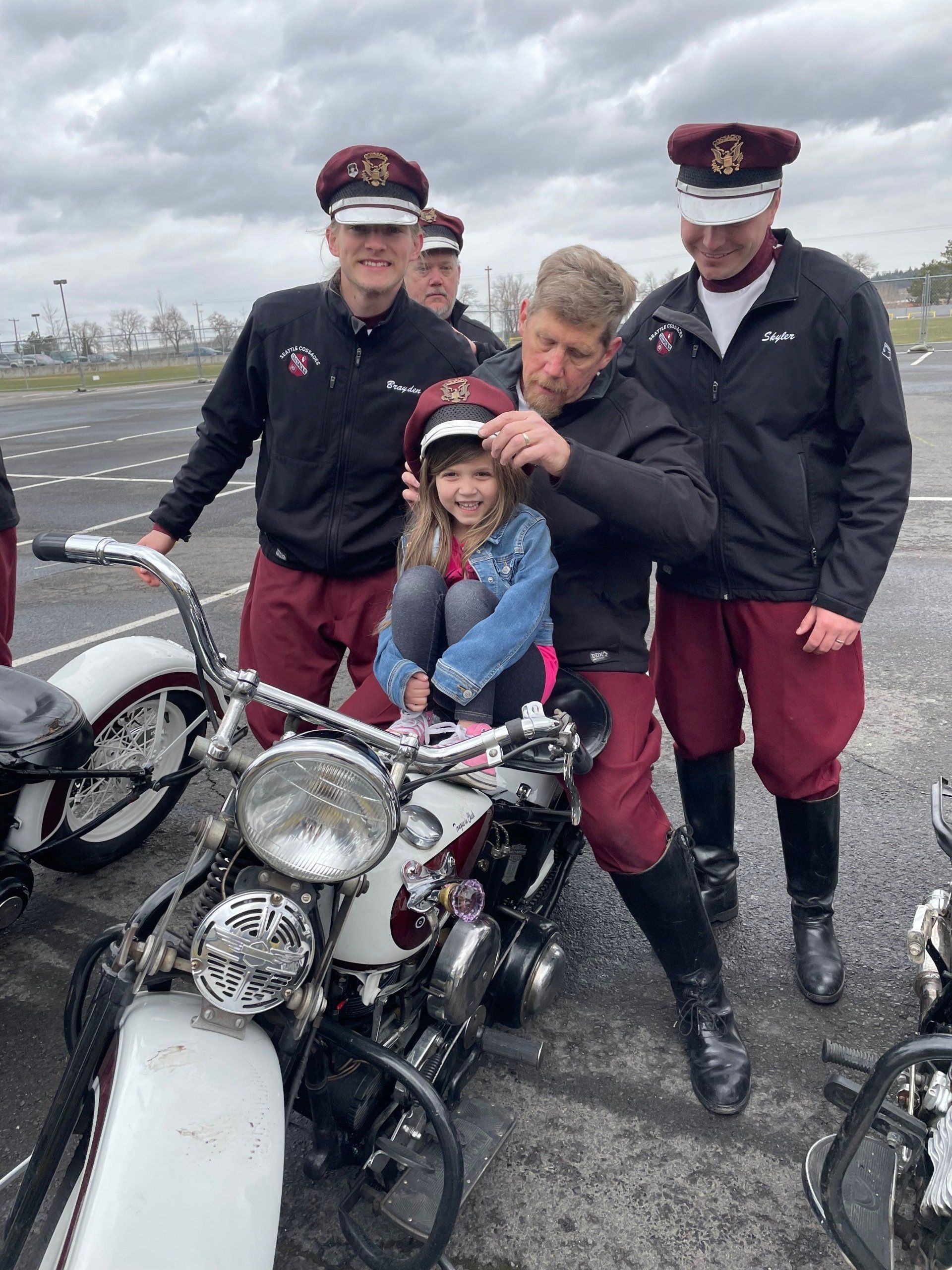 Group beside white motorcycle on wet pavement, with a child seated on the bike wearing a helmet.