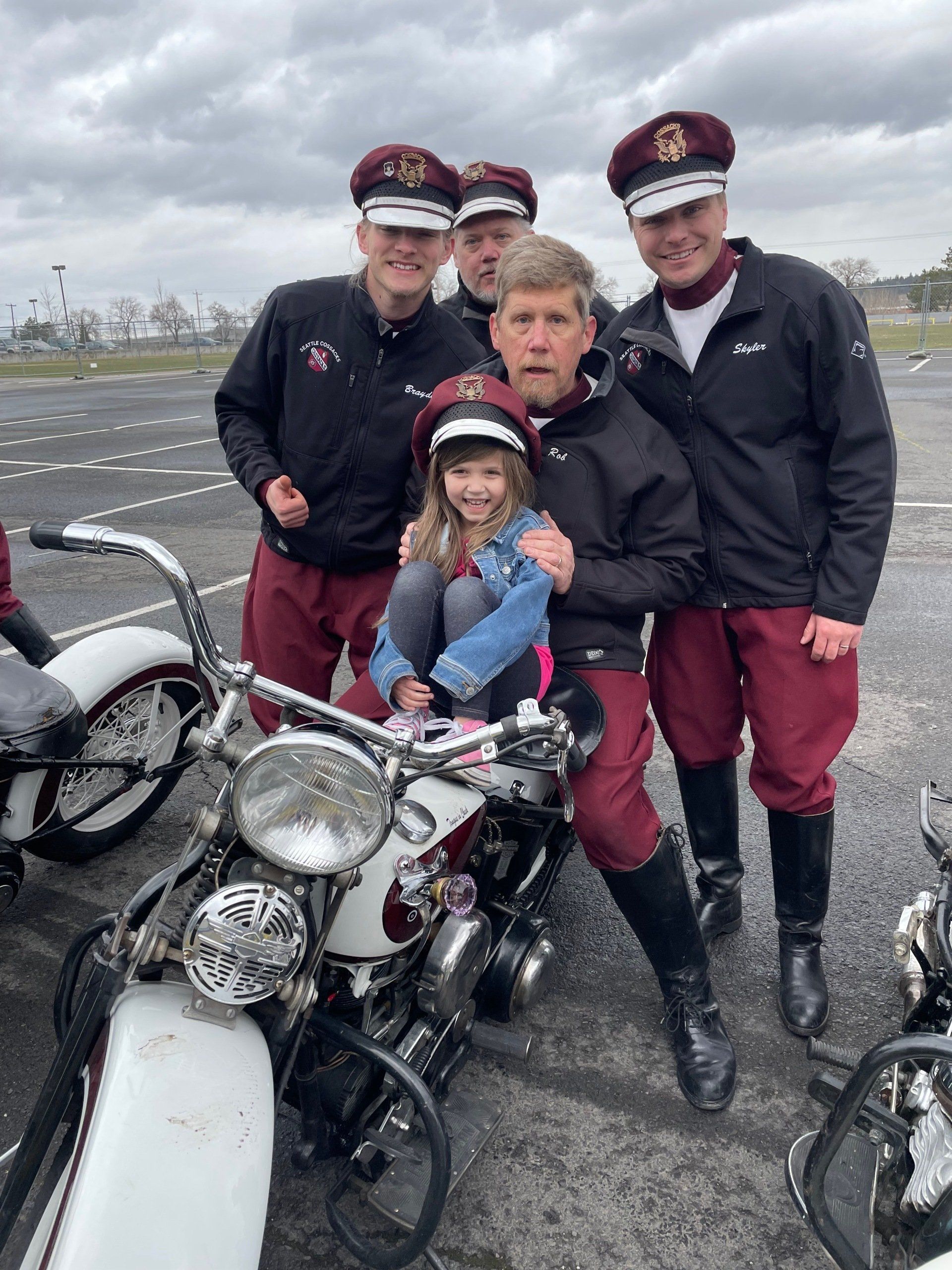 Four people pose with a motorcycle on a gray tarmac under cloudy skies.
