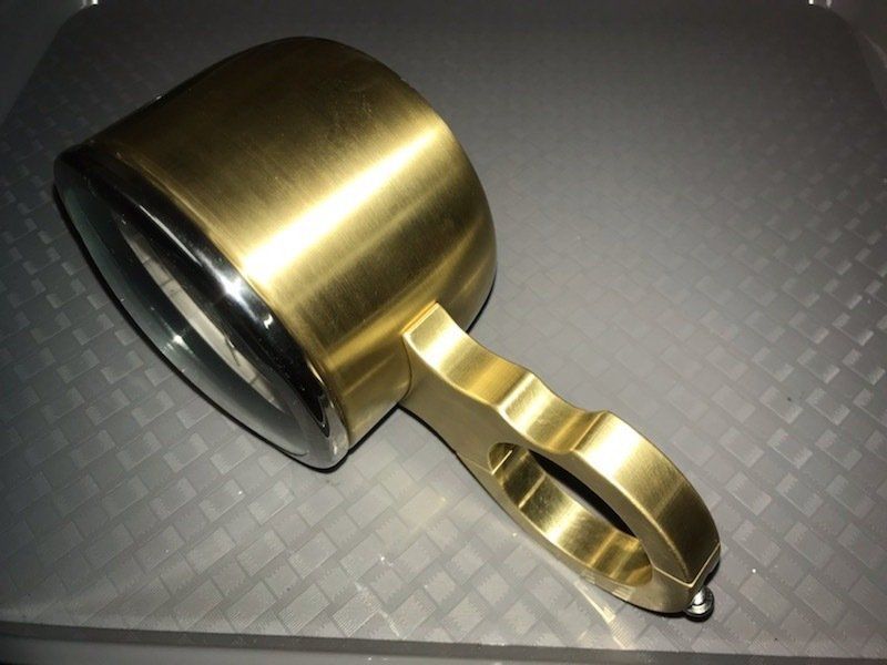 Brass-colored handheld flashlight with a black lens, lying on a gray textured surface