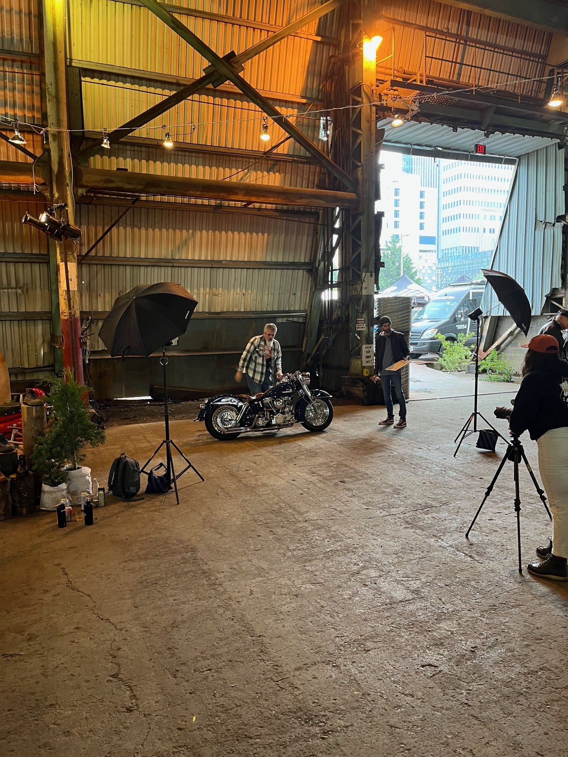 Motorcycle indoors in a rustic warehouse with lighting stands and a person near the entrance