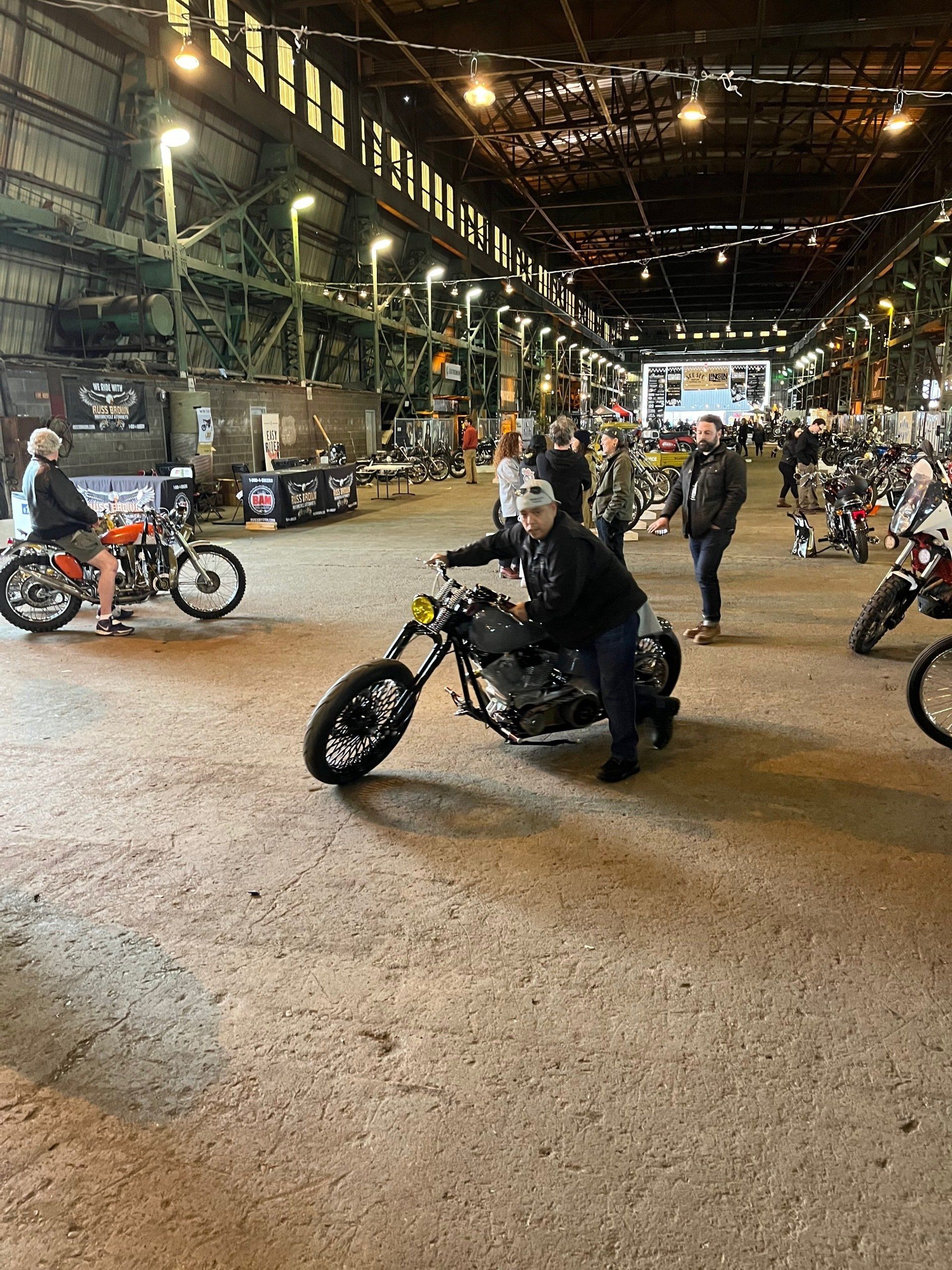 Motorcycle riders inside a large industrial hall, one leaning into a turn in the foreground.