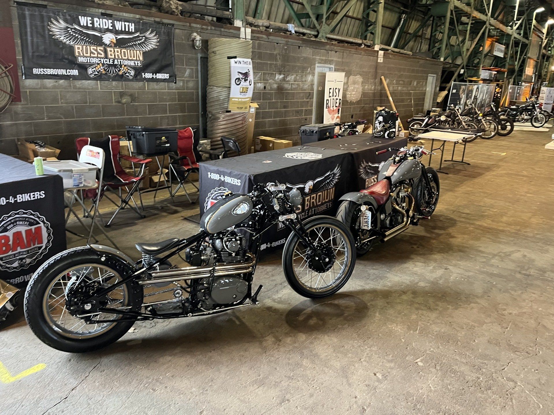 Vintage motorcycles lined up indoors at a garage, with a black drag bike in the foreground.