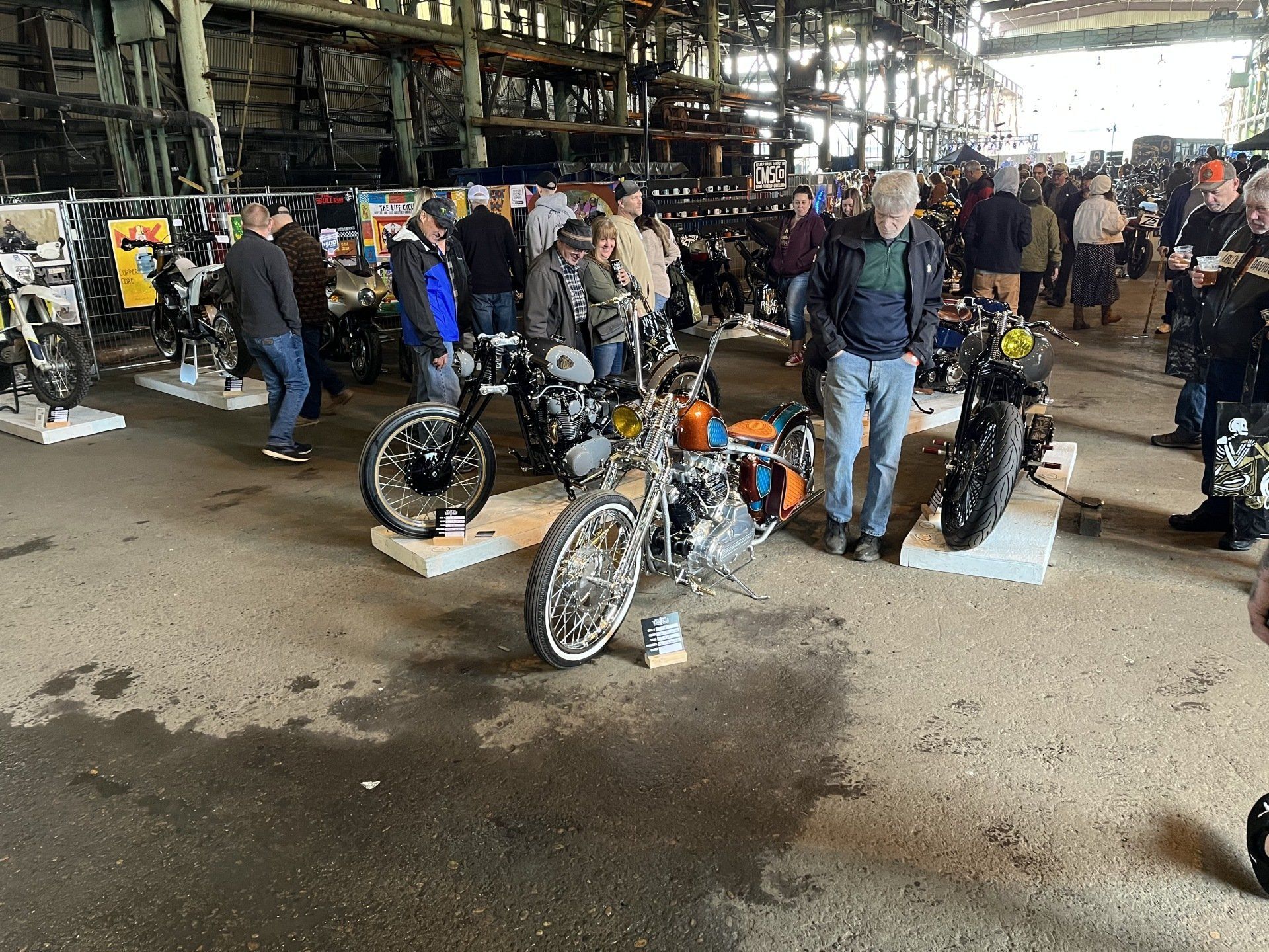 Motorcycles displayed at an indoor bike show, with people browsing in the background.
