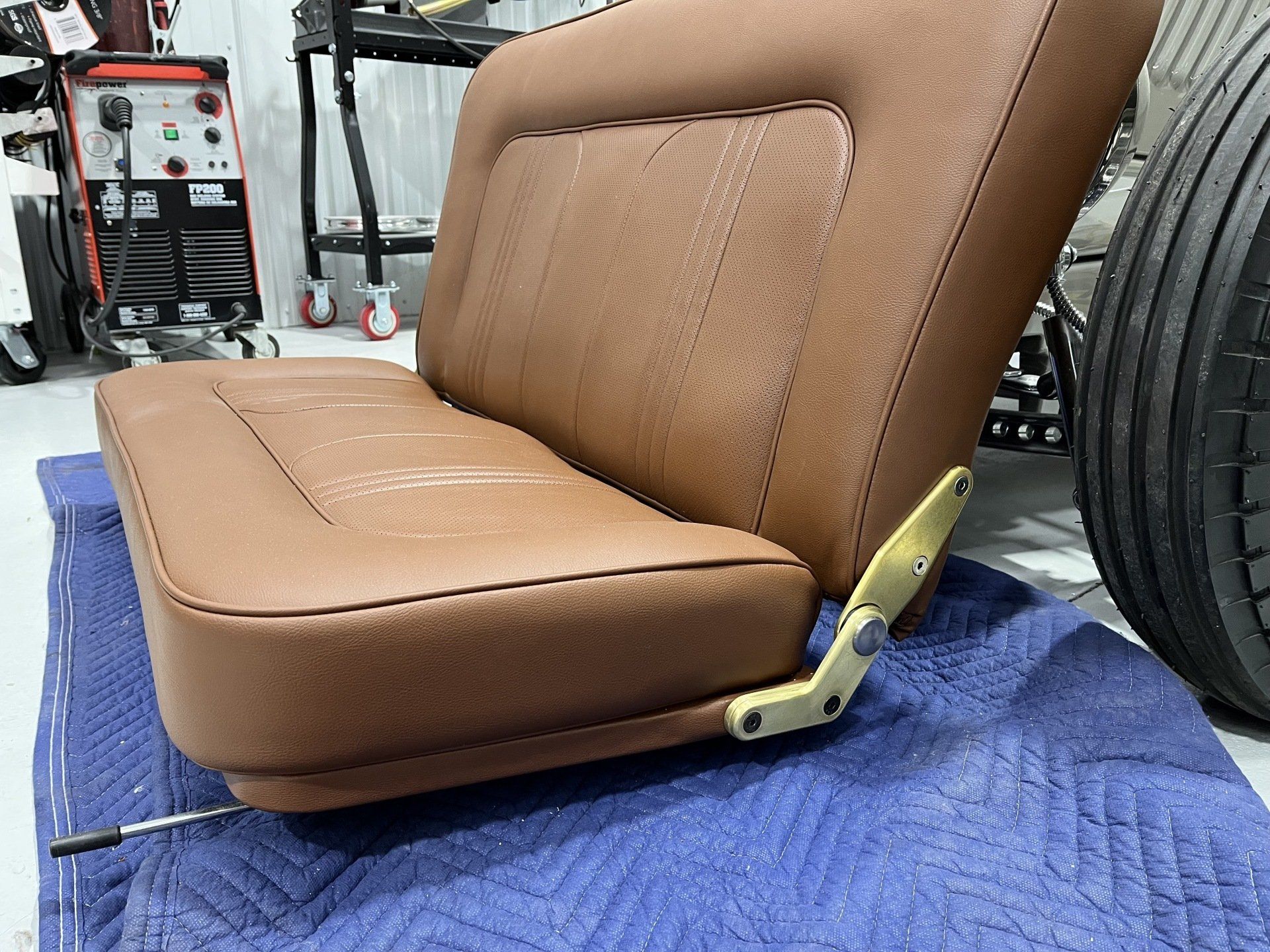 Brown vinyl tractor seat with metal bracket, resting on a blue tarp in a workshop