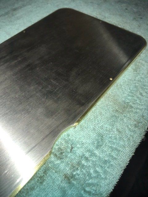 Close-up of a black metal sheet on a teal fabric surface, with a bright glare on the left edge.
