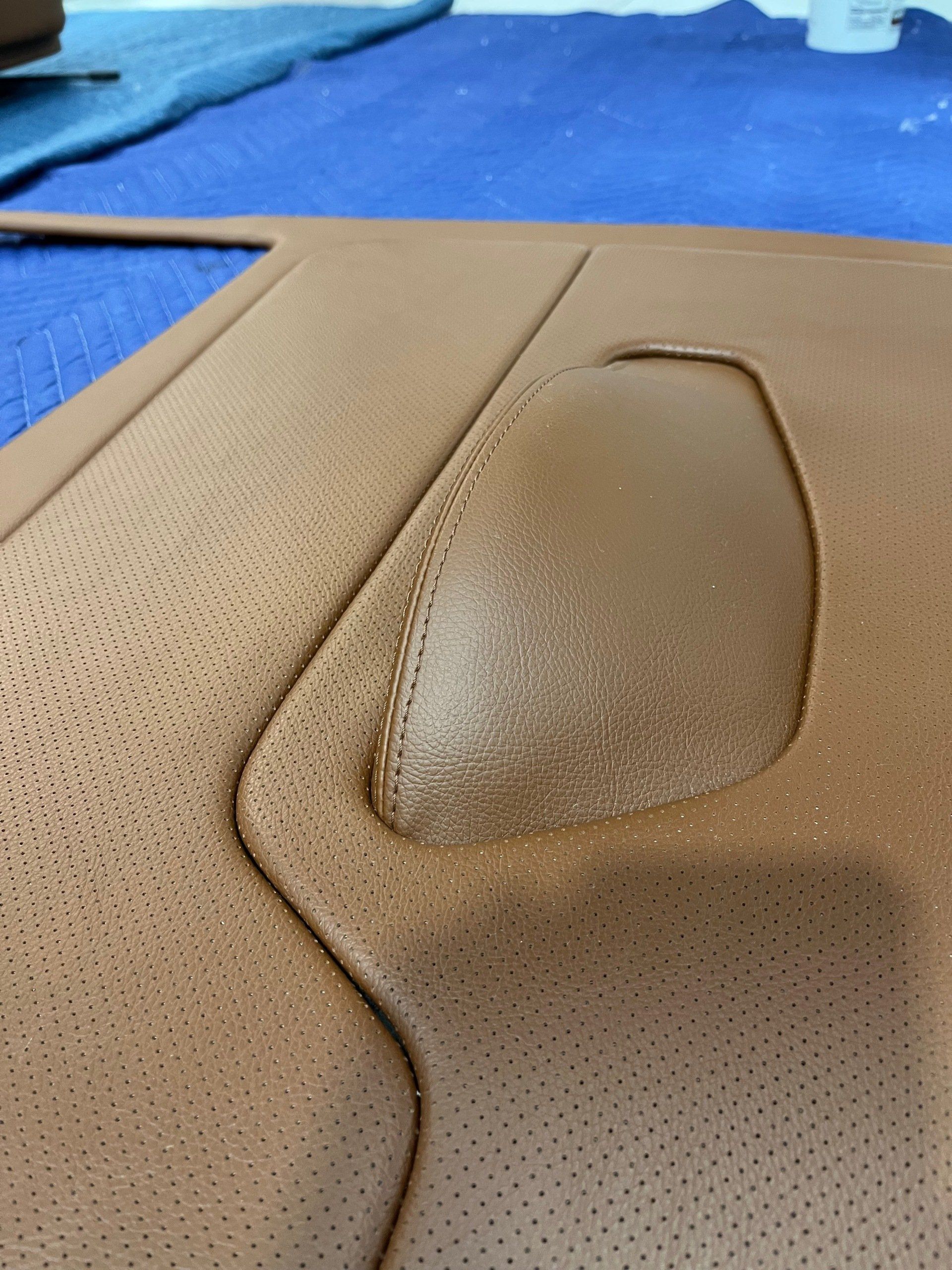 Close-up of a tan perforated leather seat with a raised worn patch near a seam