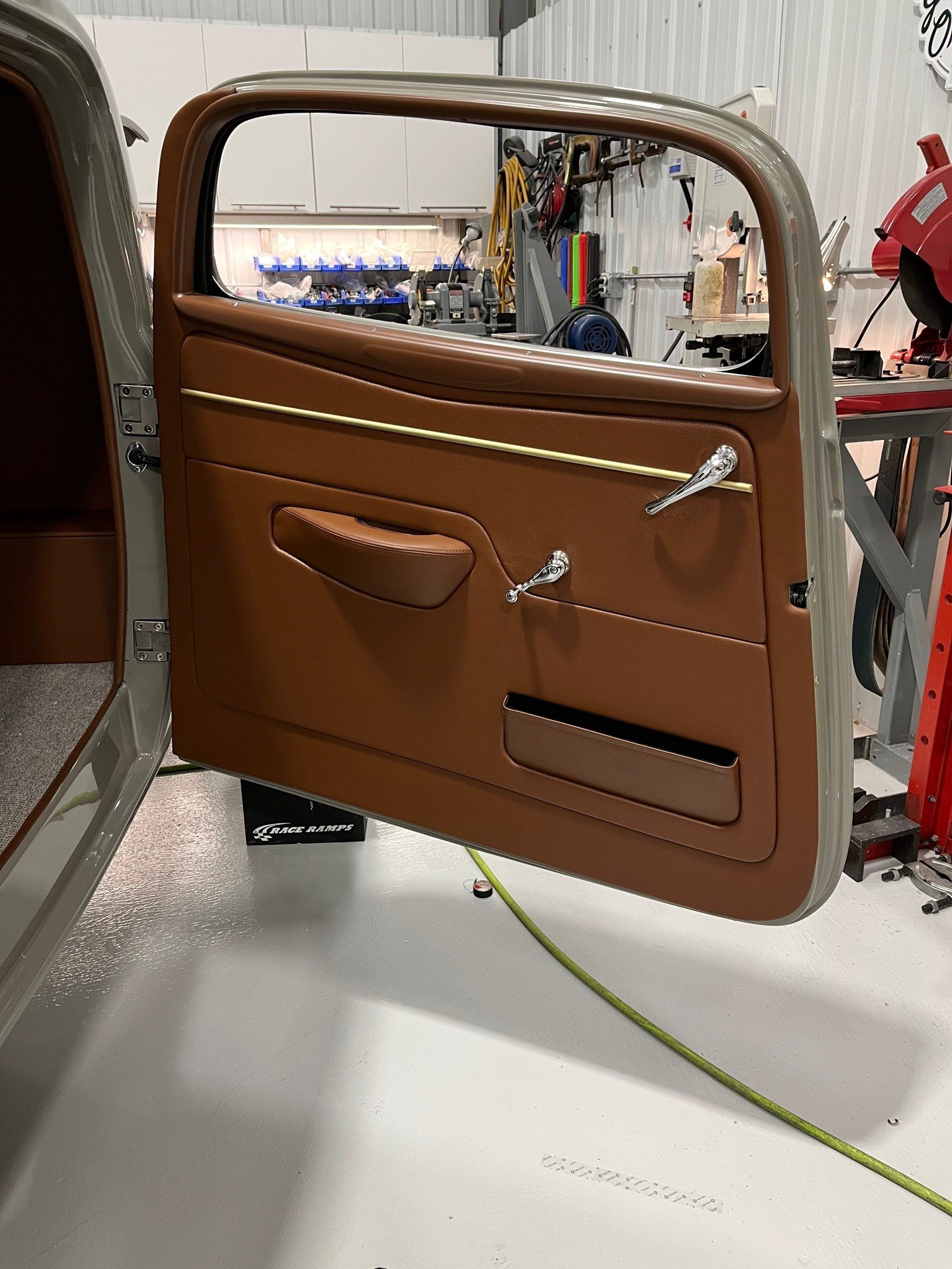 Brown leather car door panel with window frame, handle, and storage pockets on a workbench