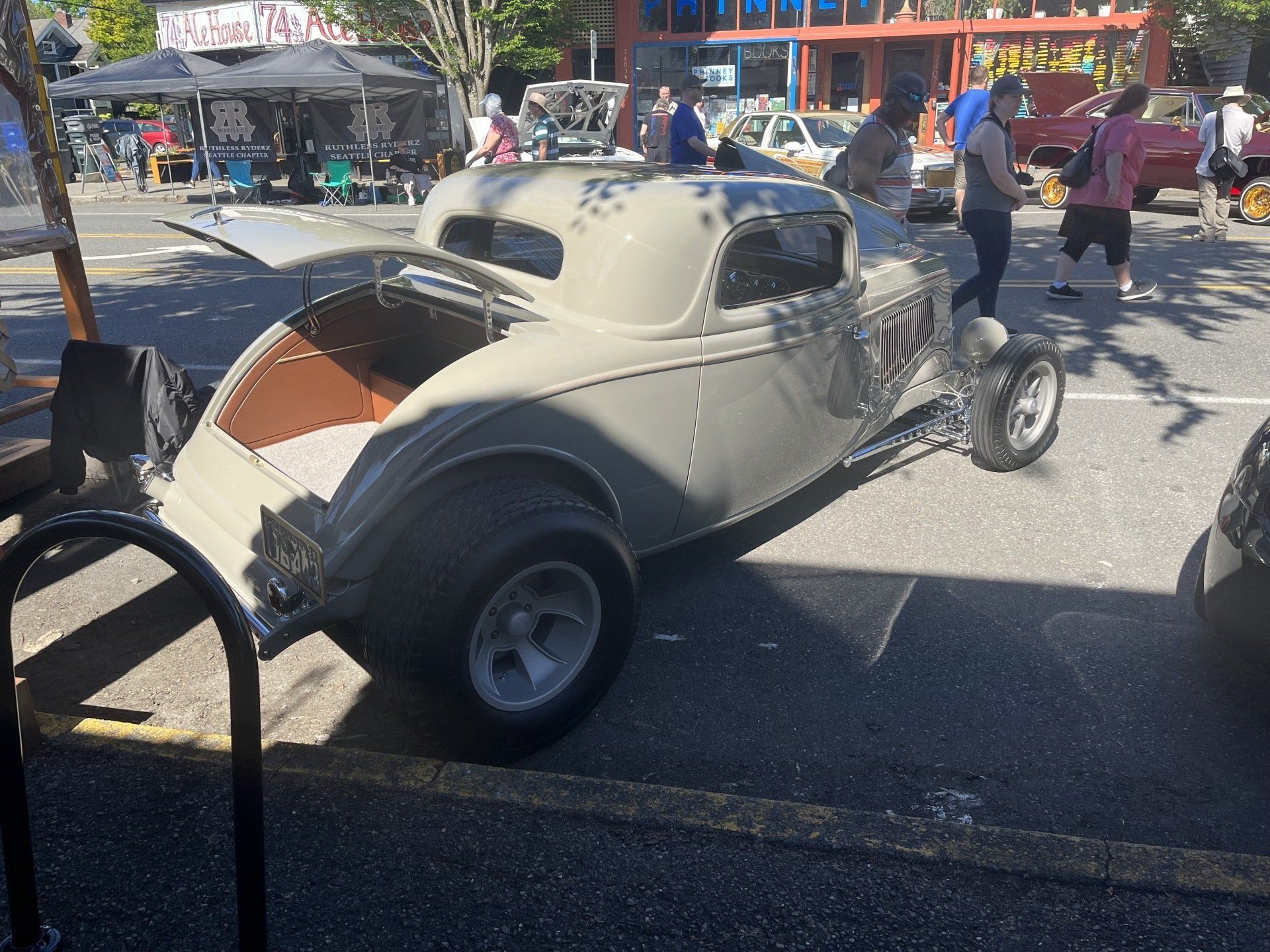 Vintage cream hot rod with exposed engine parked at a sunny car show, people in the background