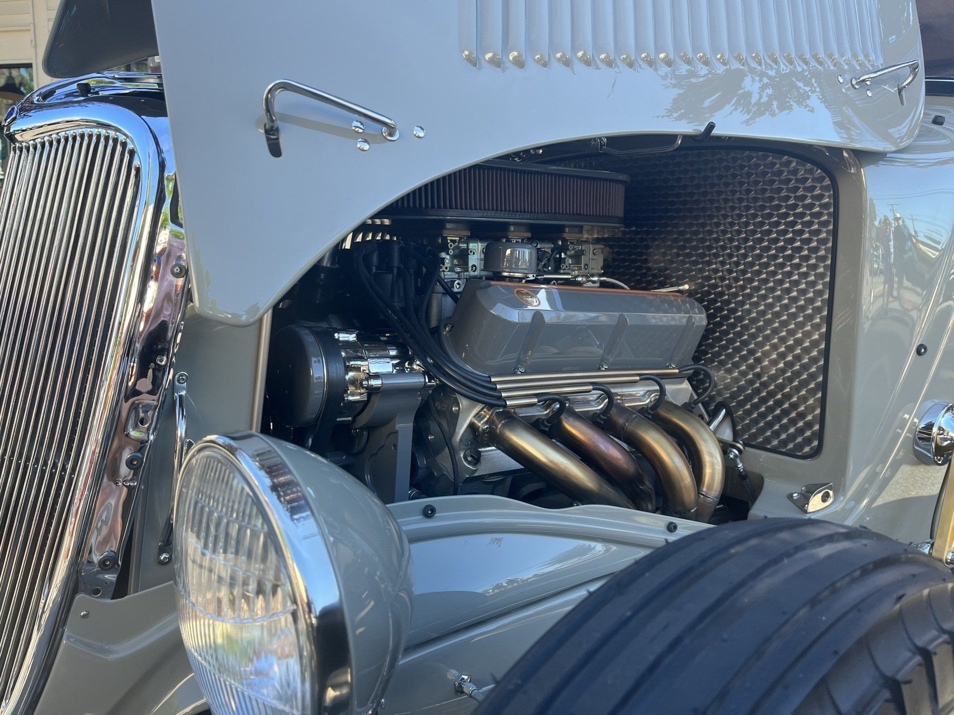 Close-up of a custom car engine with chrome parts, exhaust headers, and a large front tire