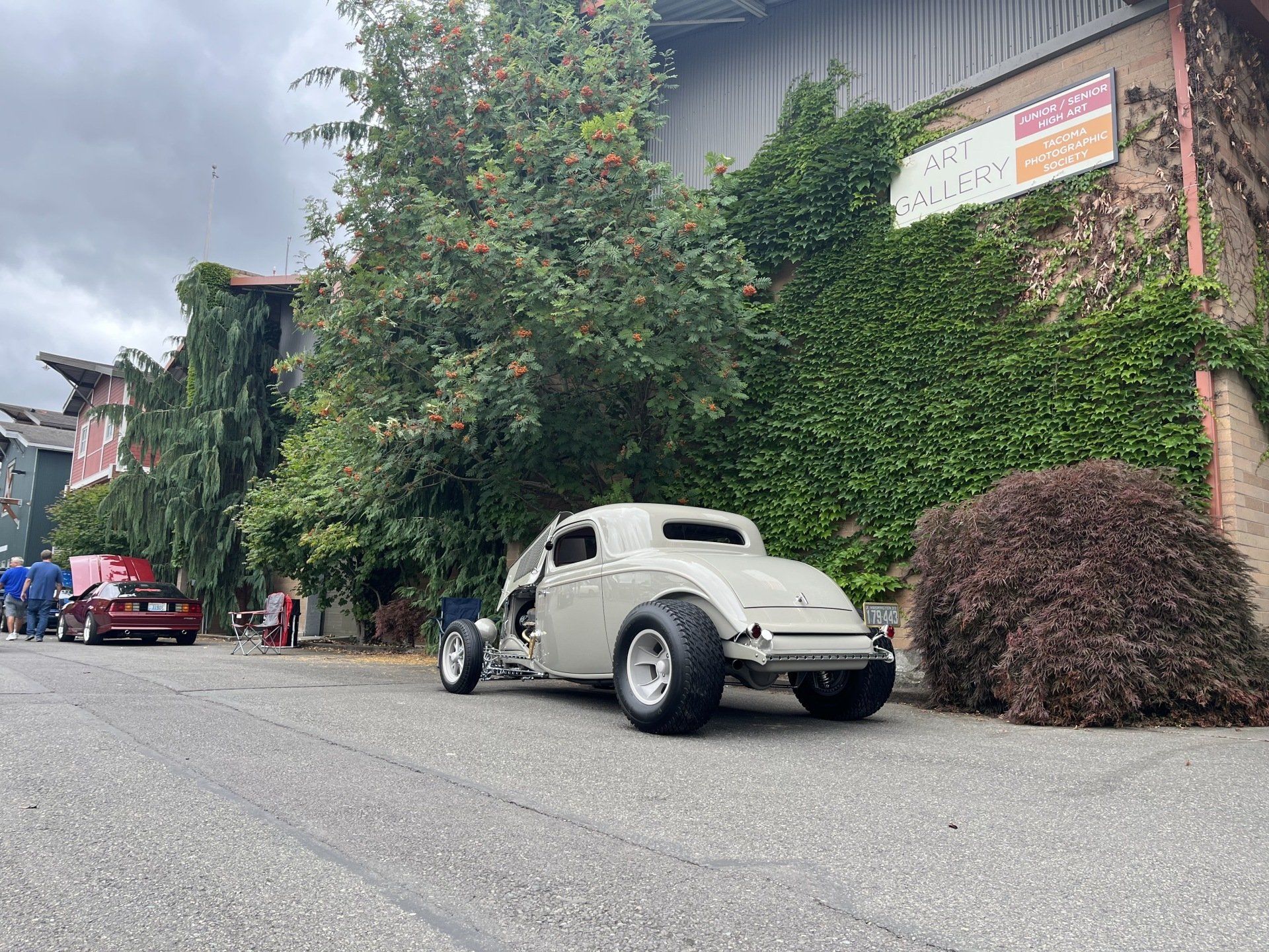 Classic cream vintage car parked beside a vine-covered building on a street.