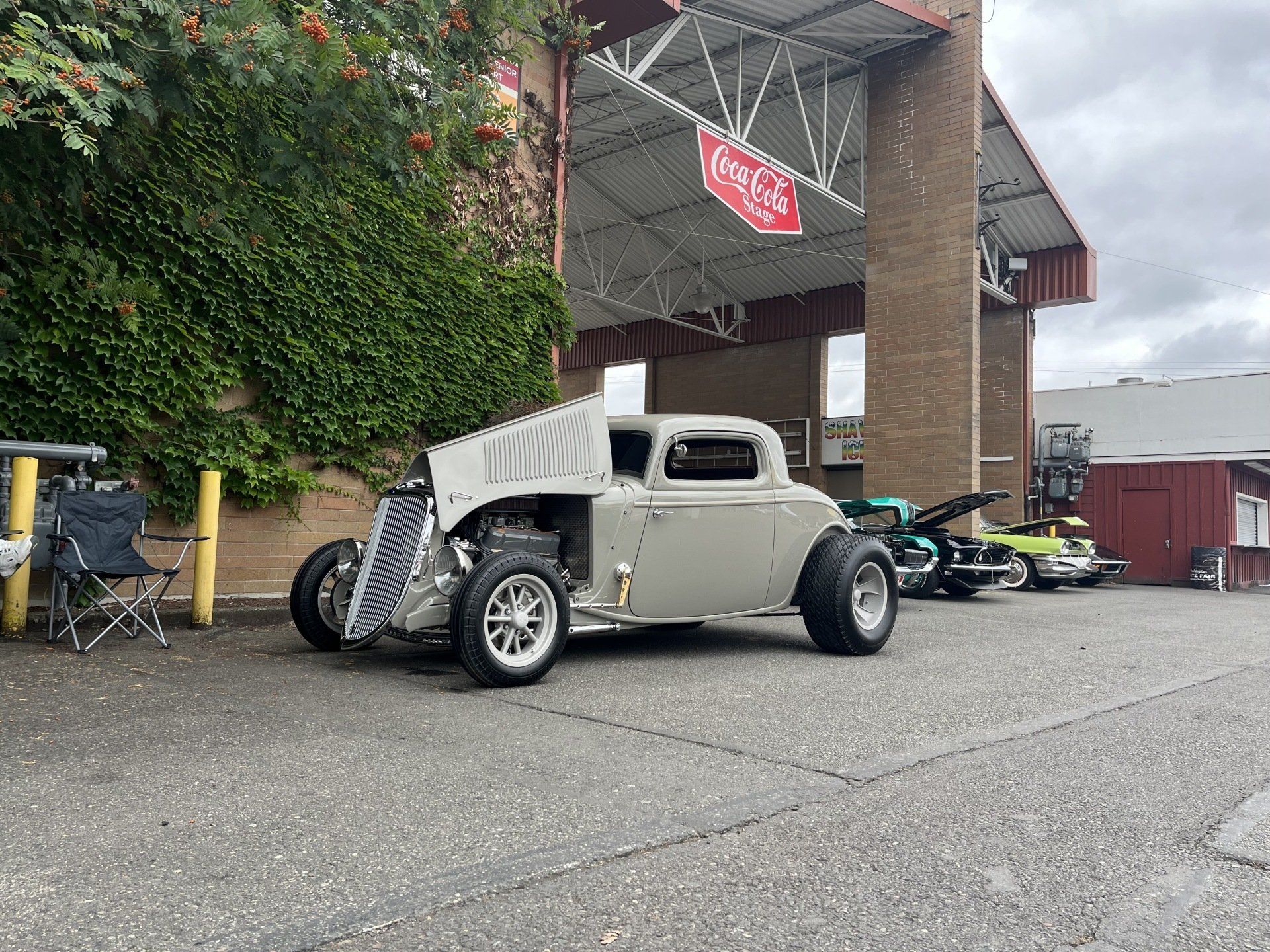 Custom vintage hot rod car parked outside a building with motorcycles in the background